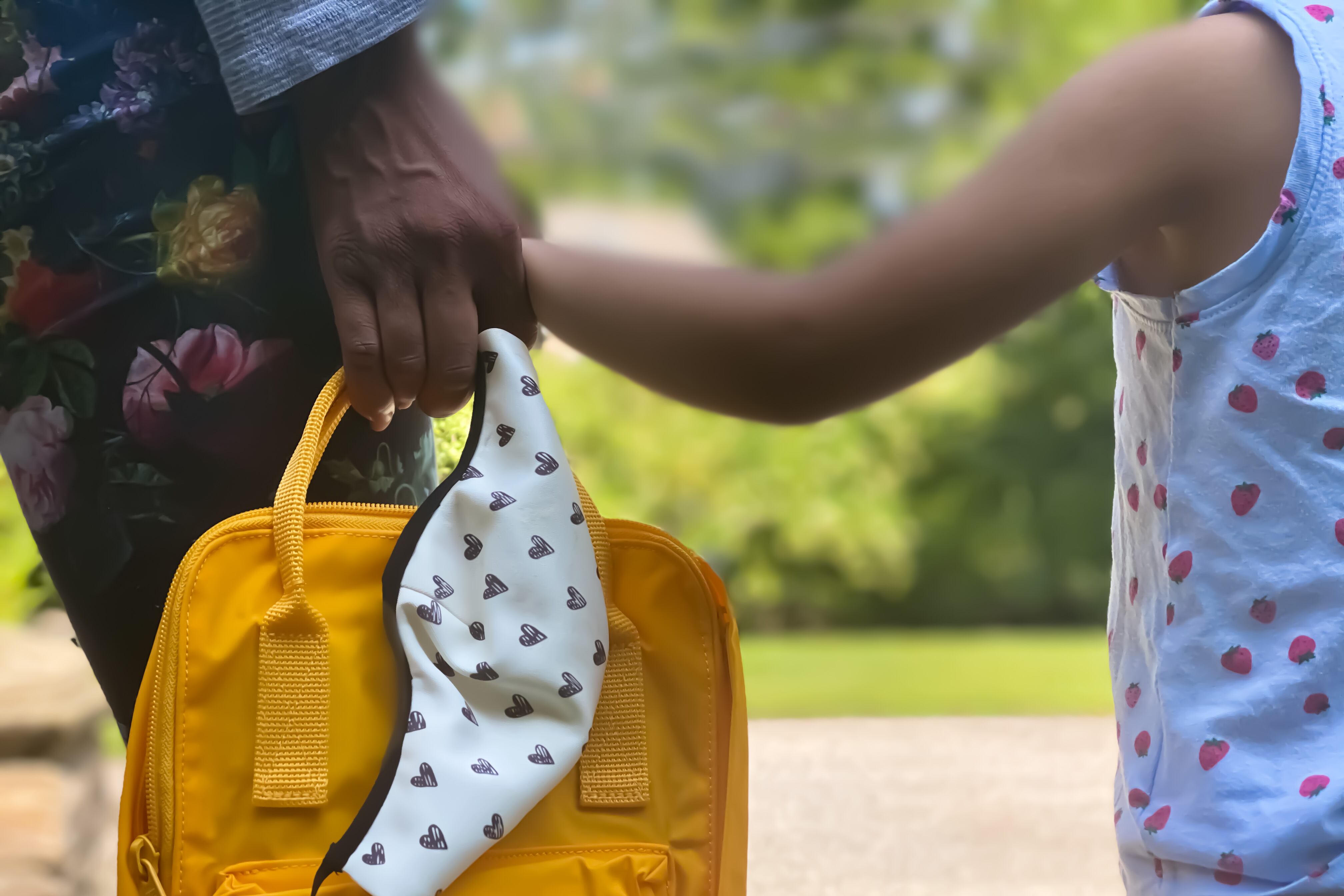 Mother and child waiting together at home for school bus with mother holding backpack and protective face mask.