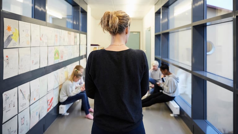 A teacher with blond hair pulled back walks down a middle school hallway.