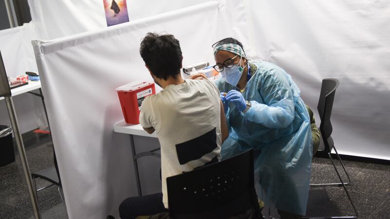 A health care professional in full protective clothing gives a dose of a COVID vaccine to a patient.