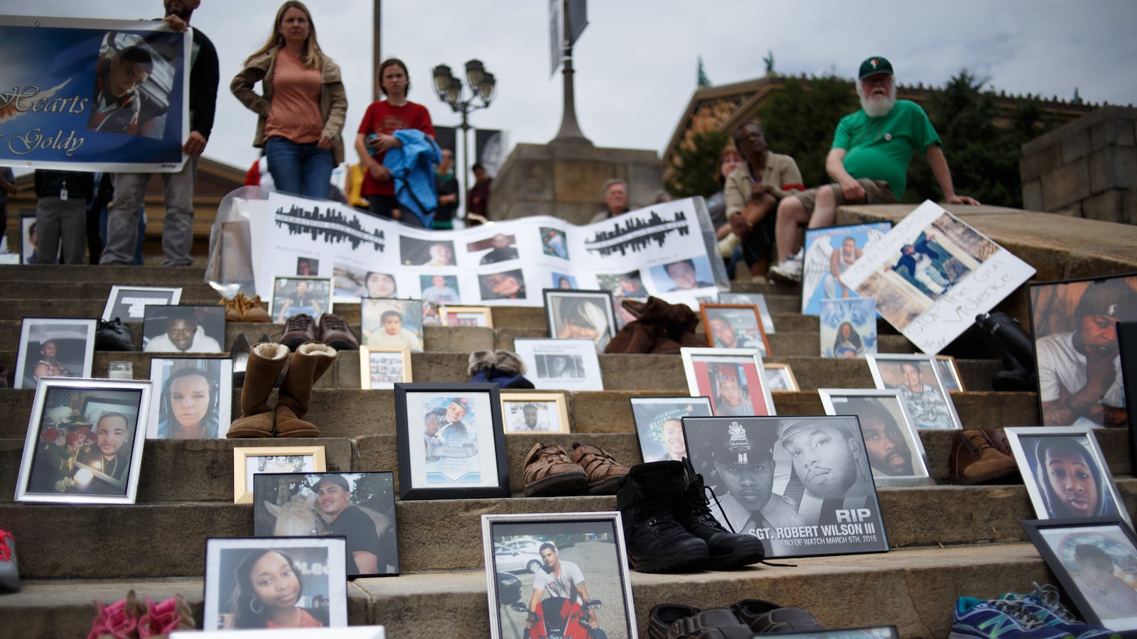 Photos of victims of gun violence line the steps as people gather around.
