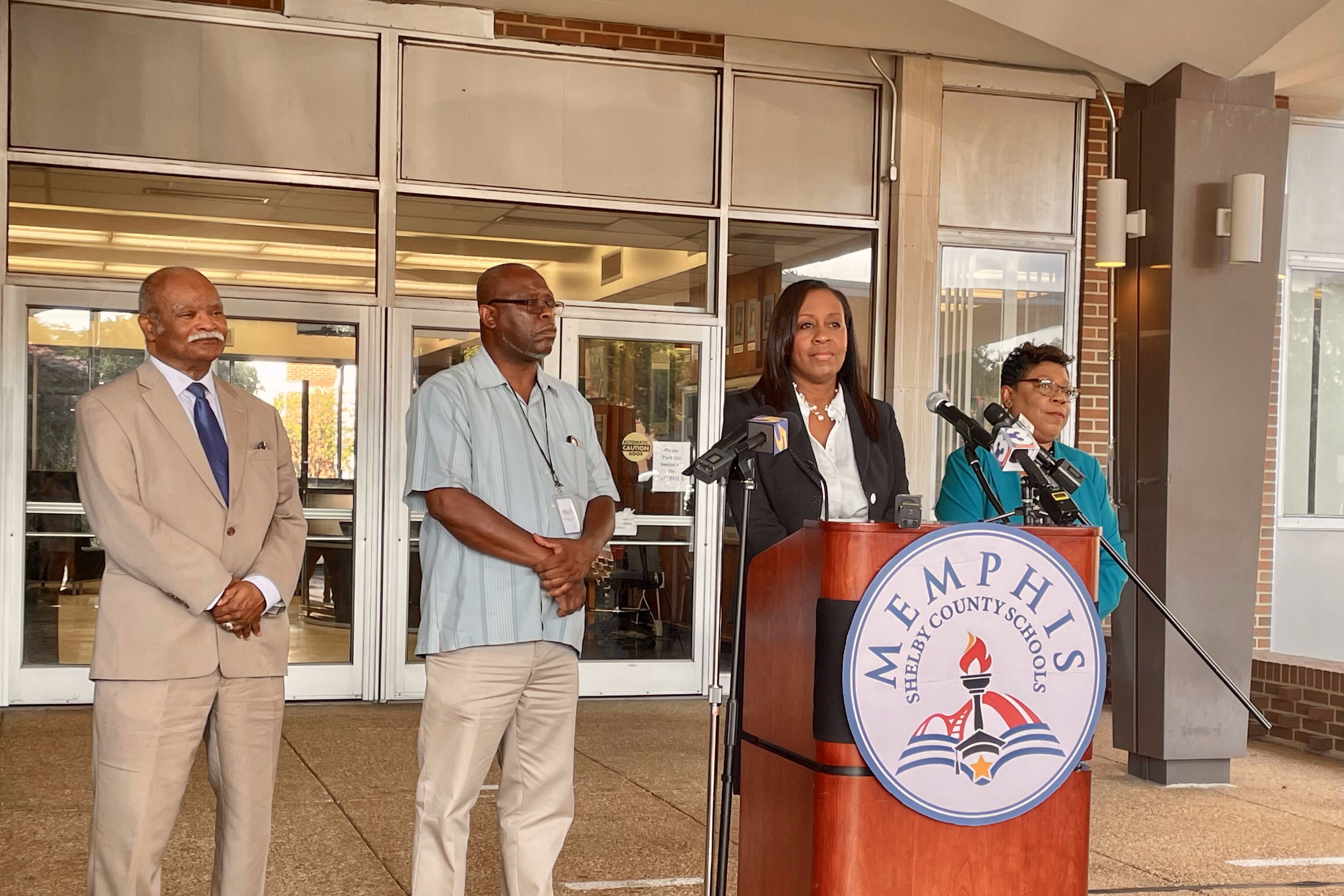 A woman stands behind a Memphis-Shelby County Schools podium next to two men and a woman