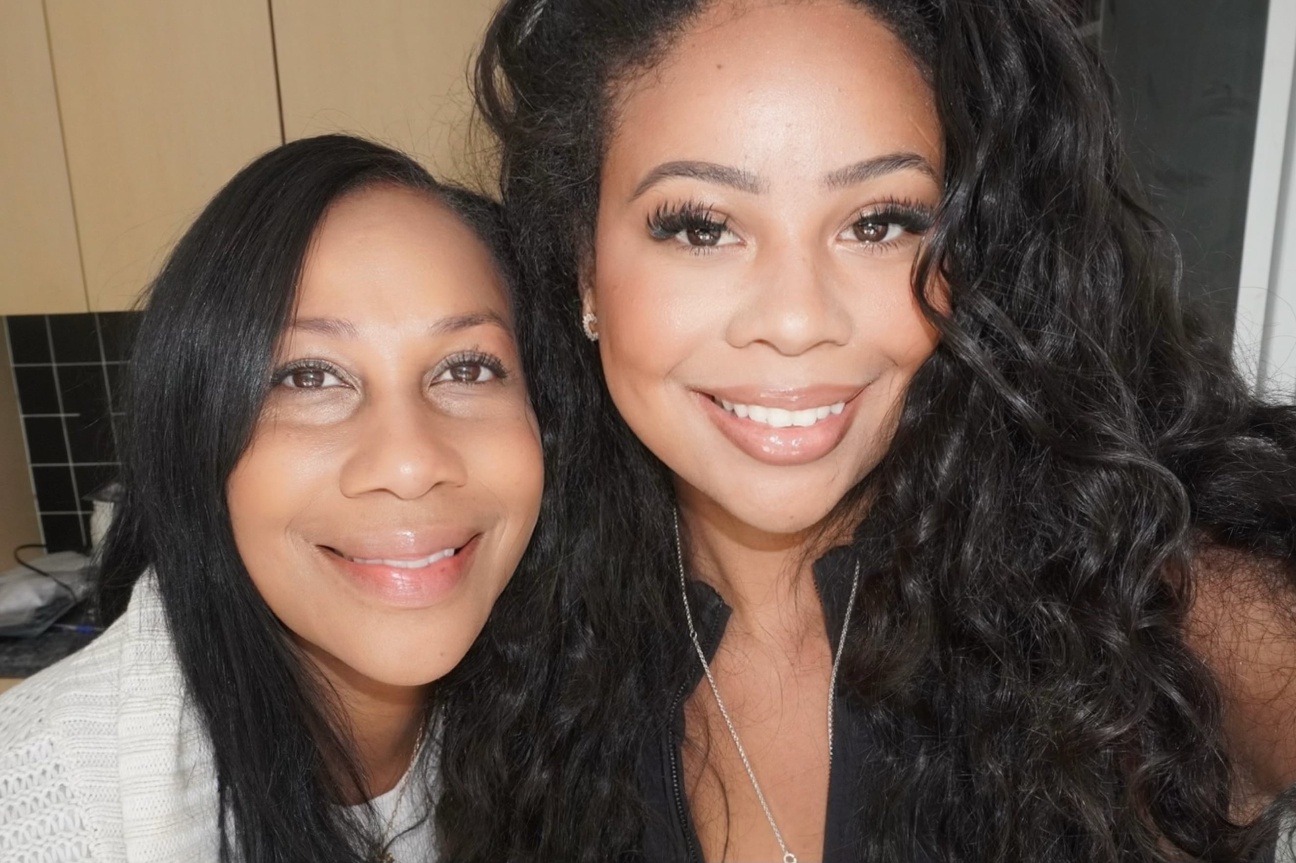 A photograph of a Black mother and her adult daughter posing for a portriat.