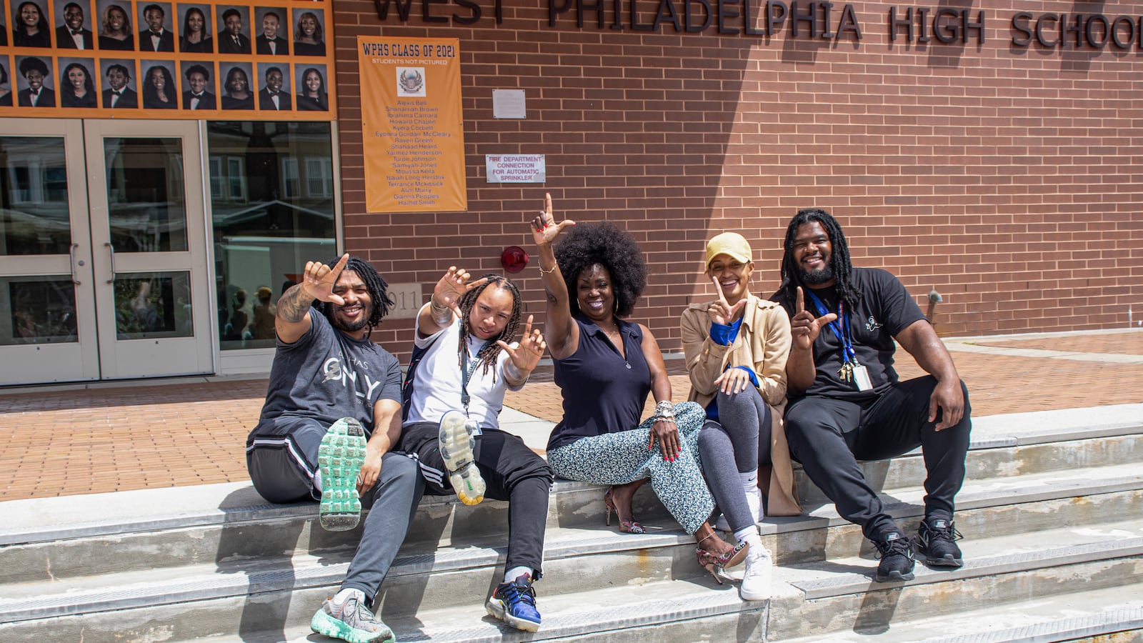 Five people pose and gesture during a portrait on the steps of West Philadelphia High School.