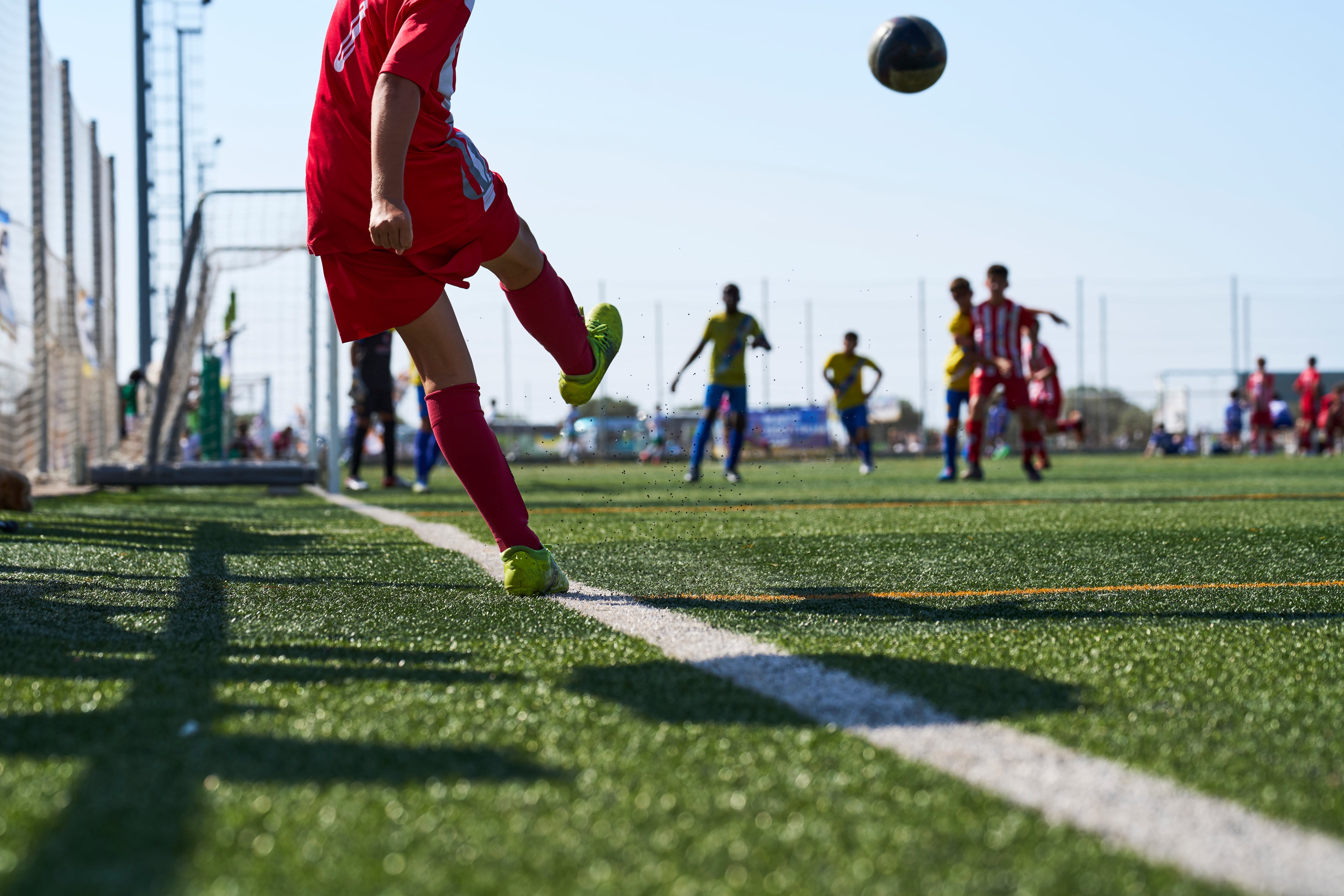 A boy in a red soccer uniform kicks the ball along the sideline.