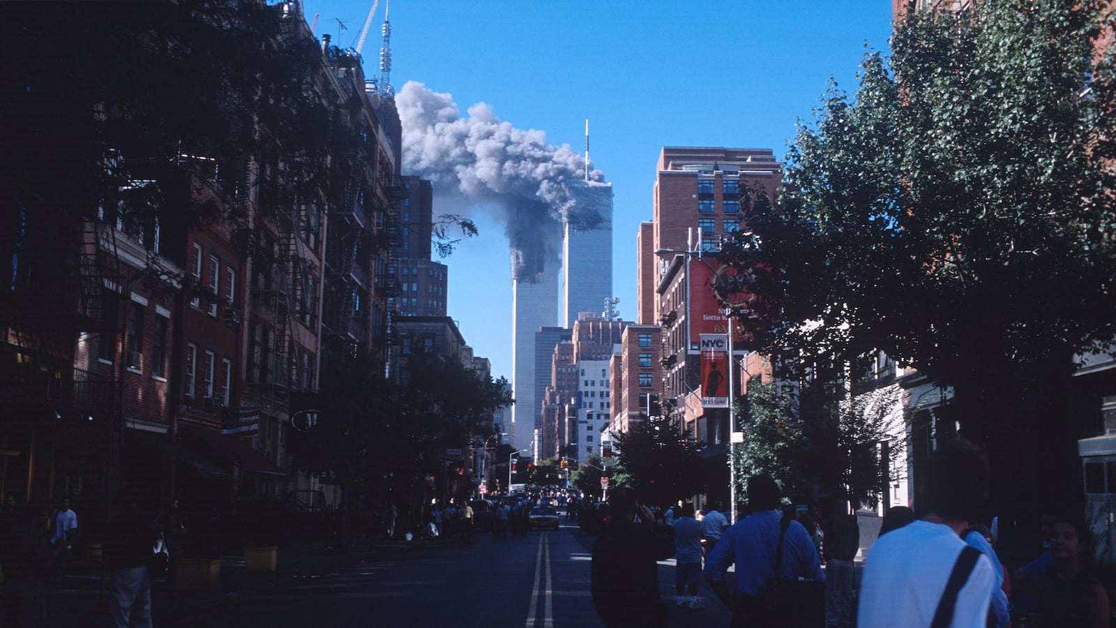 People look on as smoke from the burning World Trade Center towers fills up the downtown Manhattan skyline after both buildings were attacked by airplanes on September 11, 2001 in New York City.