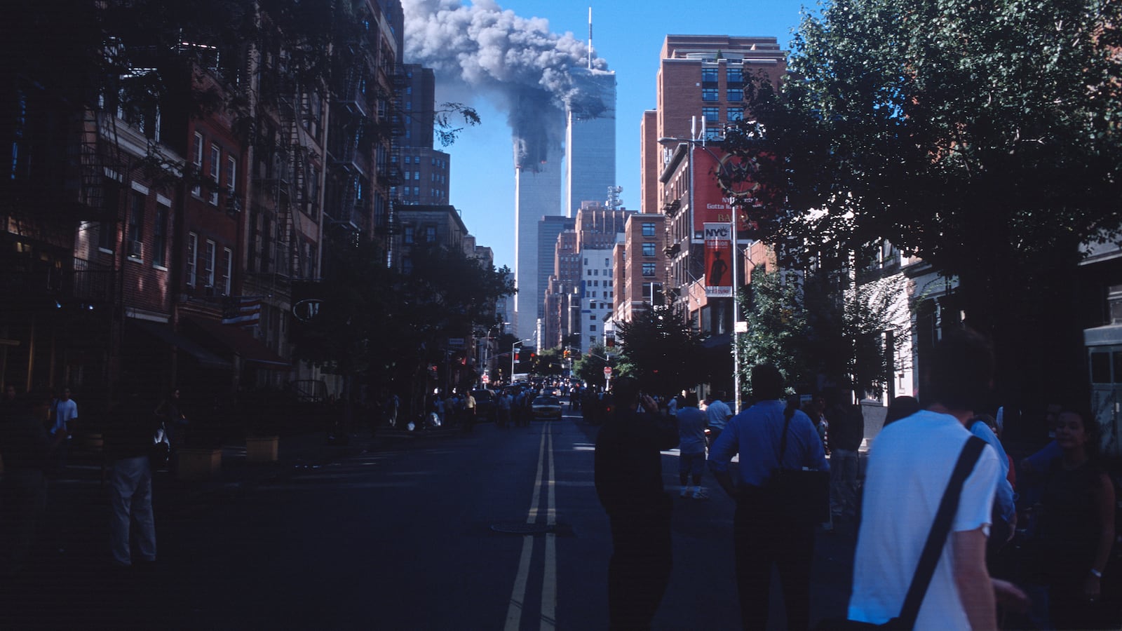 People look on as smoke from the burning World Trade Center towers fills up the downtown Manhattan skyline after both buildings were attacked by airplanes on September 11, 2001 in New York City.