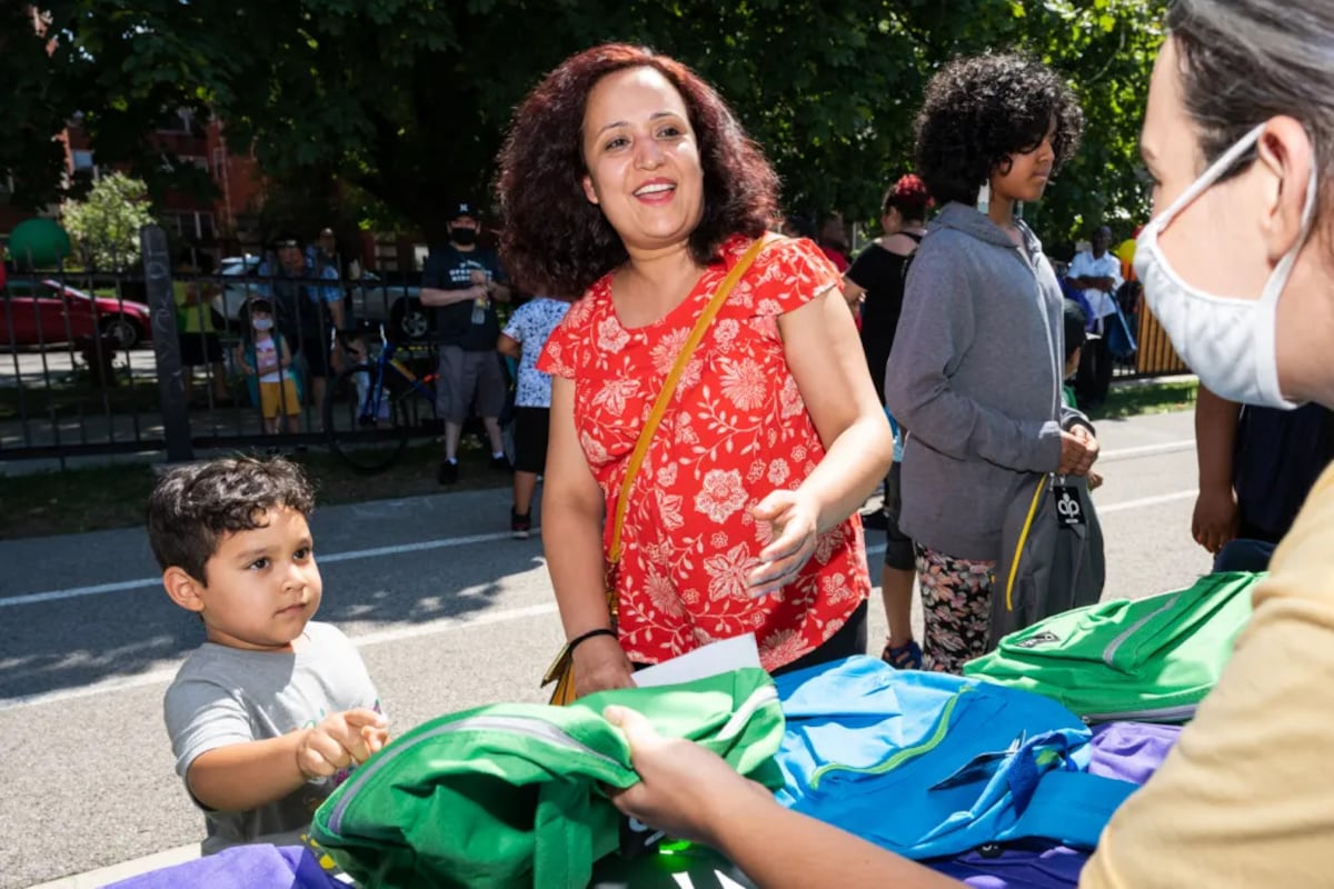 A woman in a red shirt and a young boy pick out a free green backpack at a back-to-school event in Chicago.