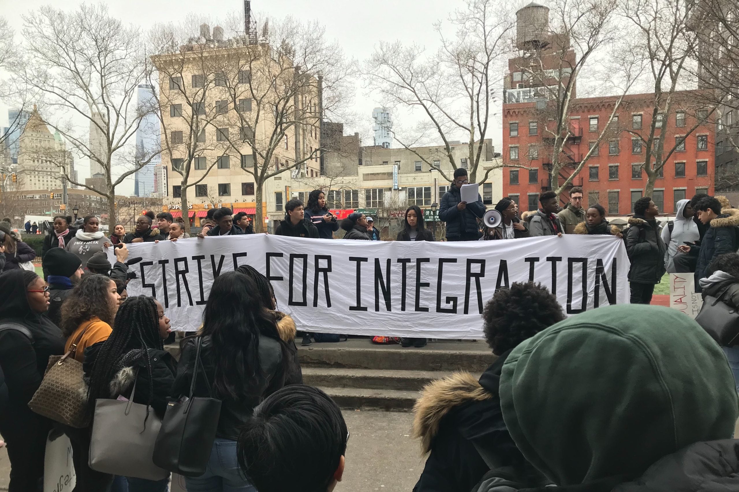 Students stand outside, some holding a large white banner.