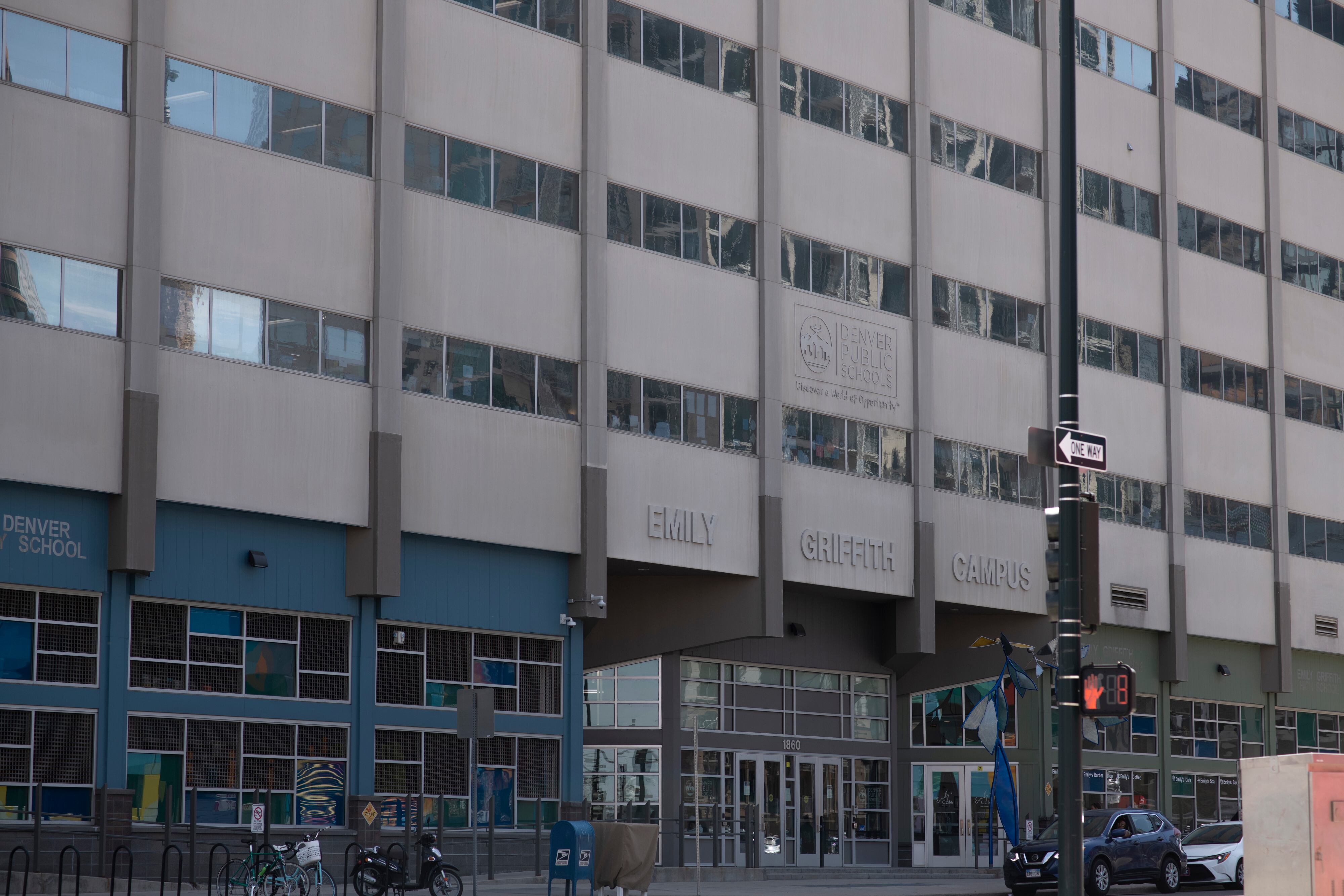 The partial front of a gray high-rise building, with windows reflecting another building, and multi-paned windows on the first floor.