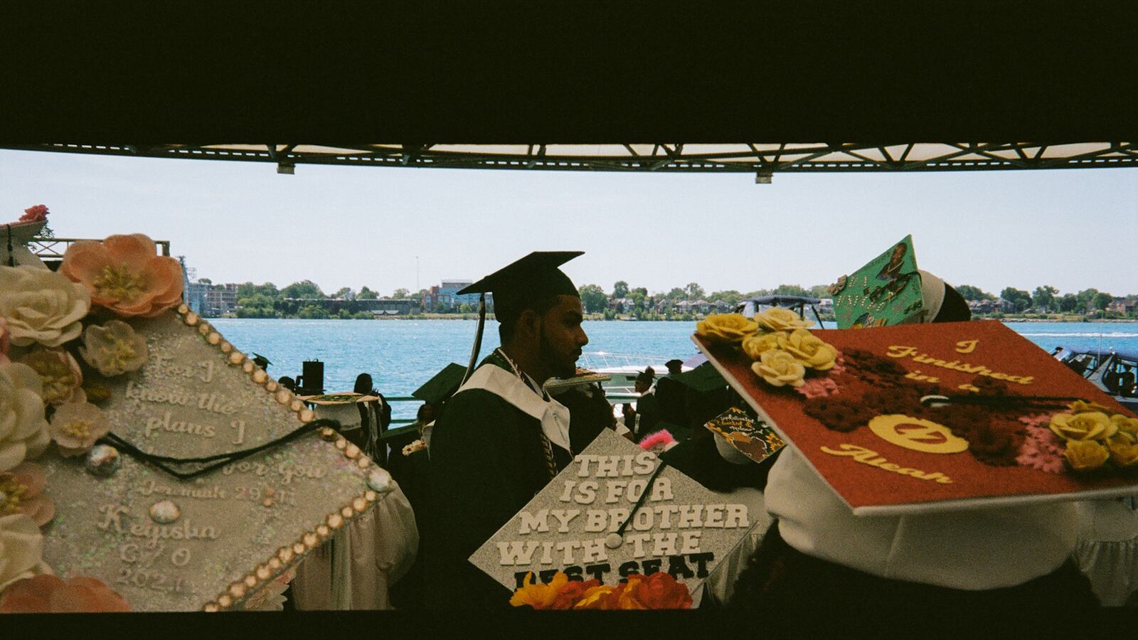 A young man walks by a group of young women, all about to graduate. The caps of the young women are all beautifully adorned with phrases, flowers and pearls.