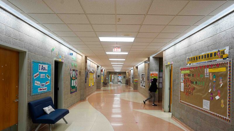 A school hallway with one student walking into a classroom door. The walls are covered in bulletin boards and art.