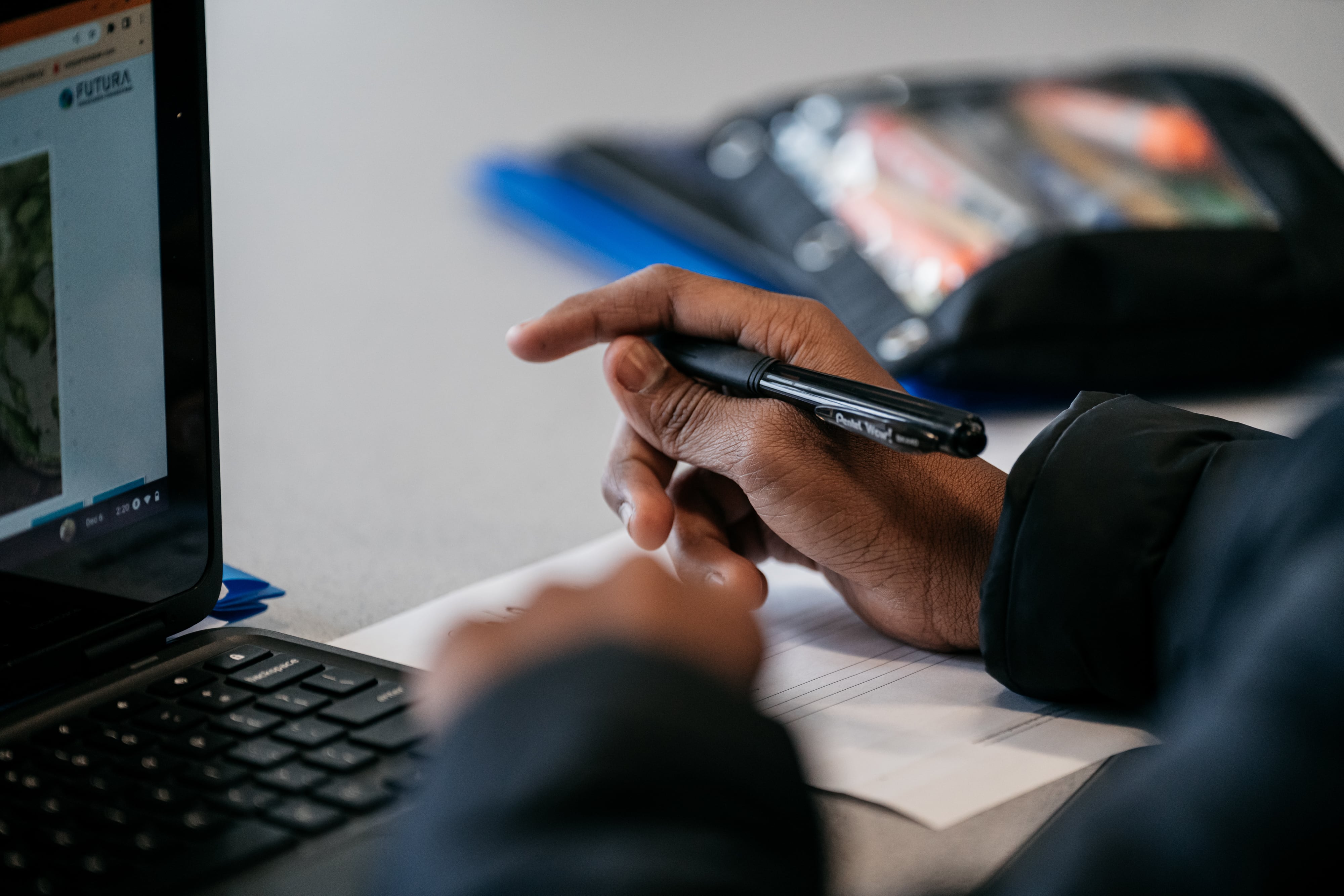 A hand is holding a pen in front of a computer screen.