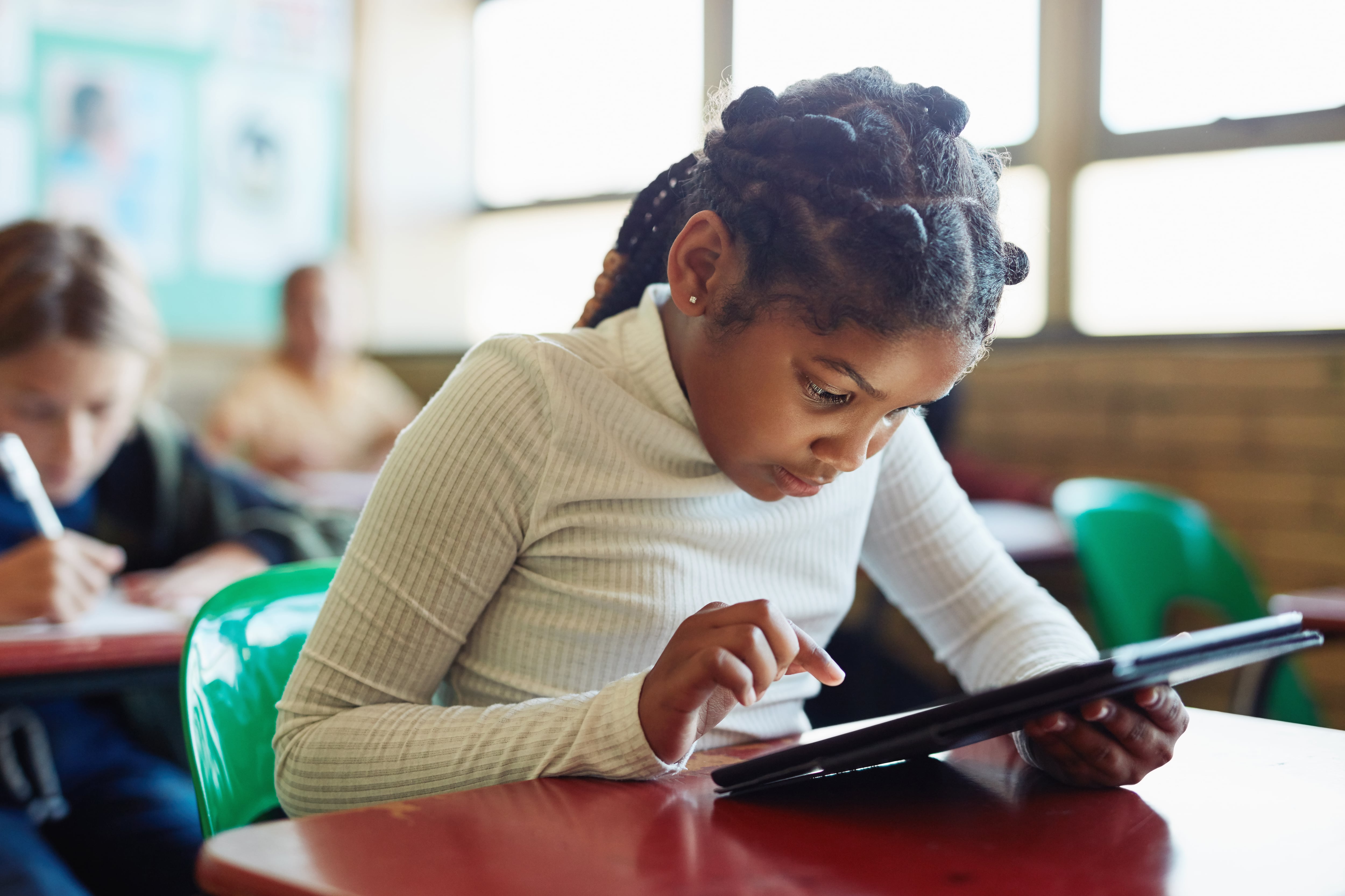 young girl using a digital tablet at her desk in a classroom