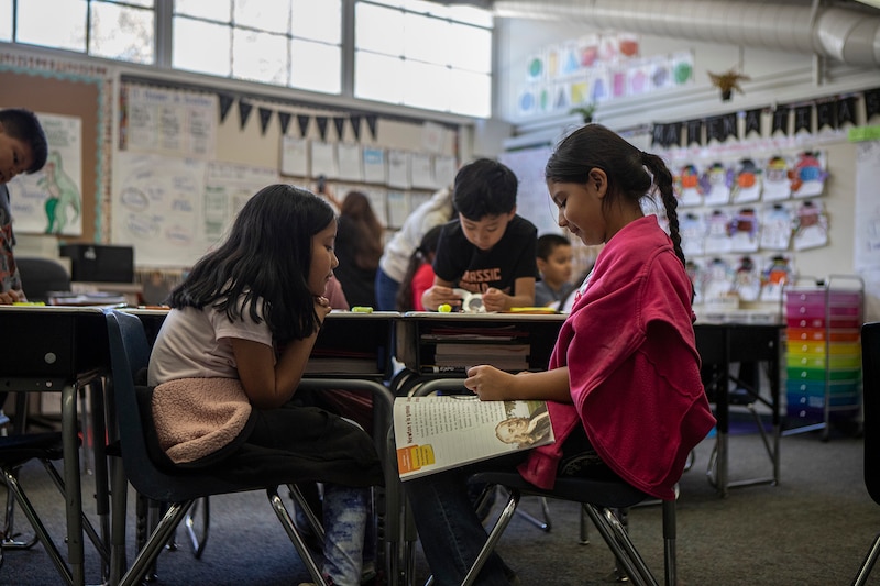 Two female students and a male student work at a table in a classroom.