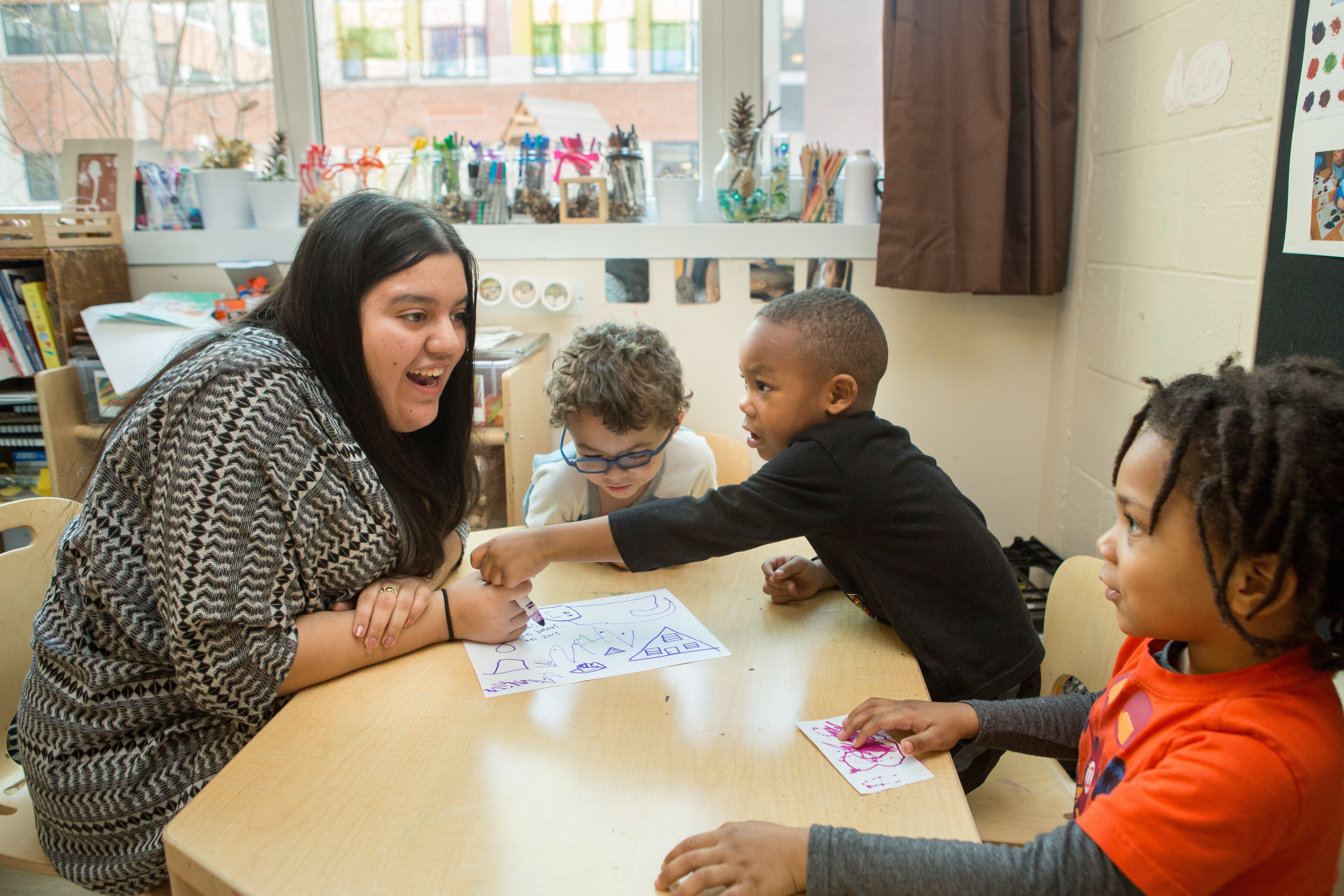 A teacher sits around a table with three young students.