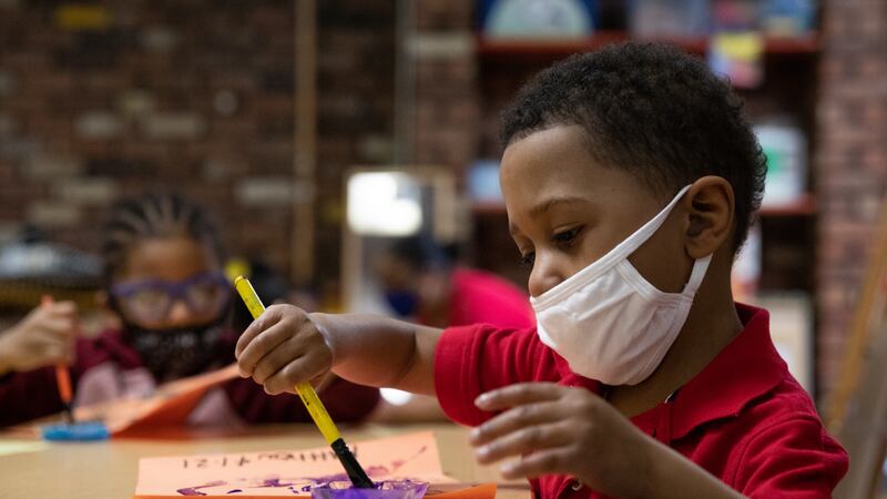 A young boy sitting in front of a piece of paper dips his brush in paint while at a preschool class.
