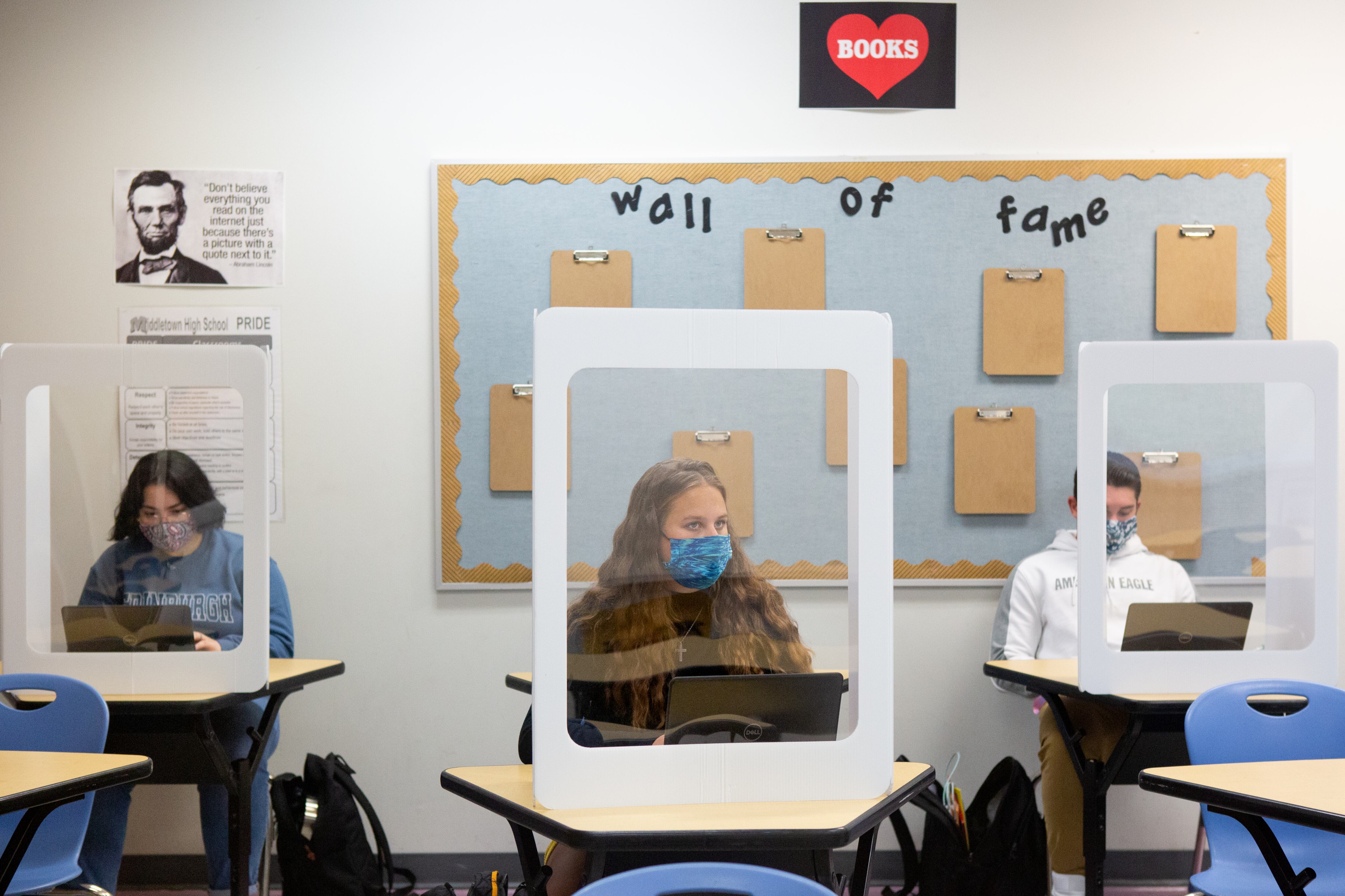 Student wearing a face masks seated behind desk shields.
