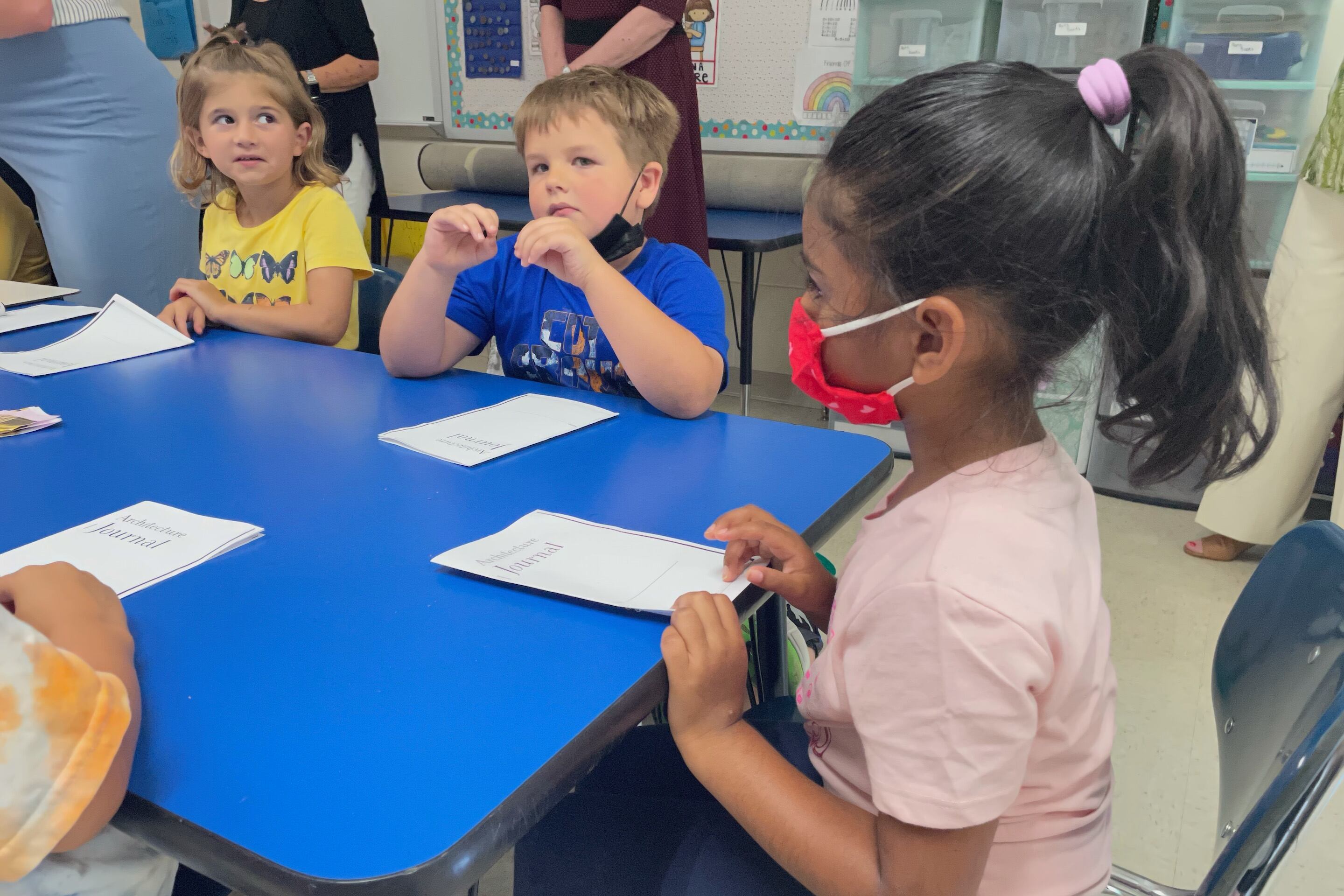 Students, both masked and unmasked, sit together at a blue table.