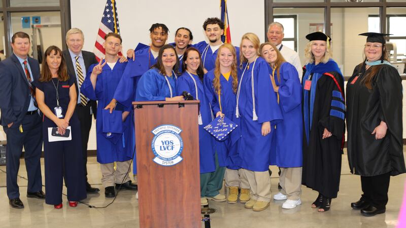 Students in blue caps and gowns and teachers in ceremonial graduation clothes pose for a picture.
