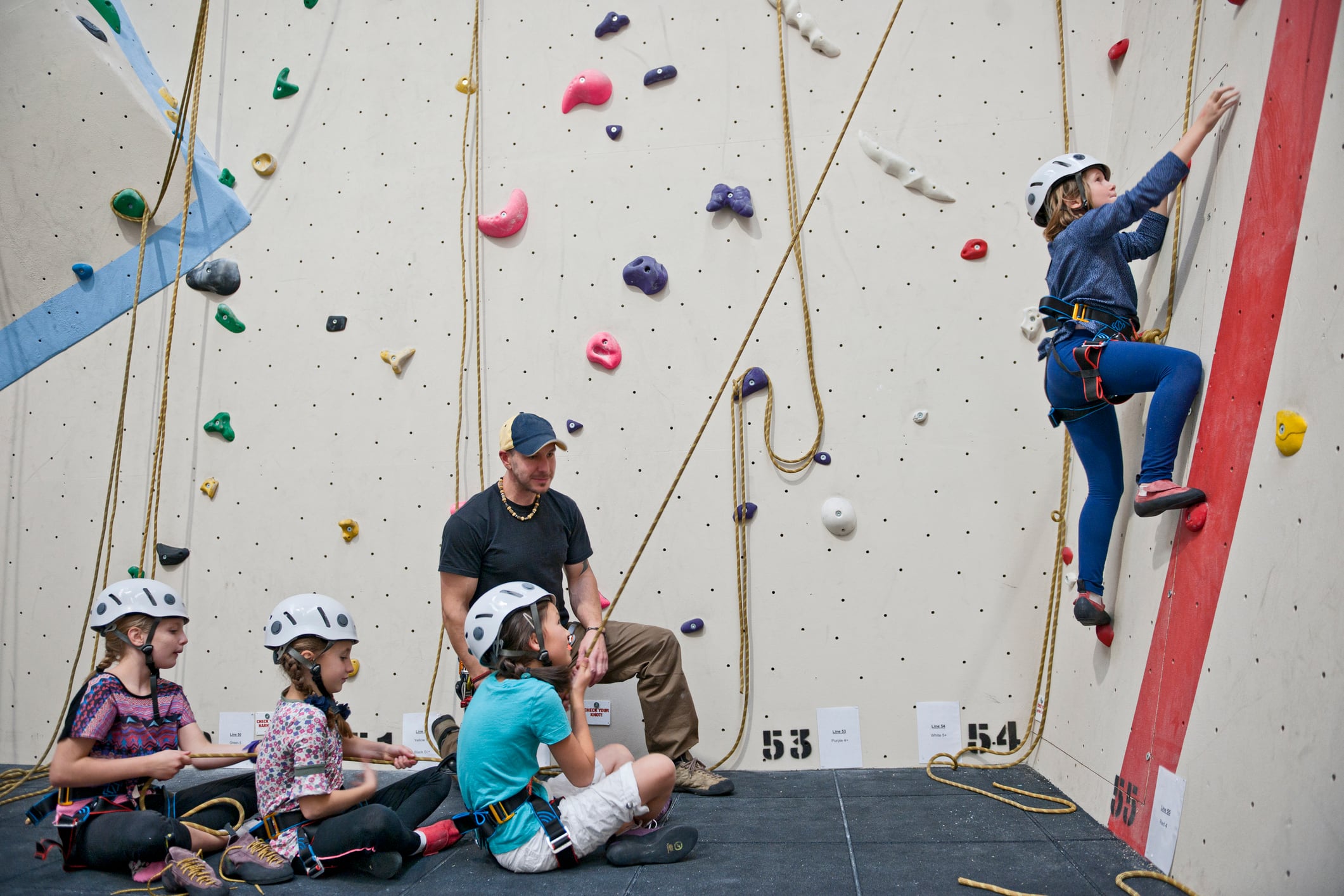 climbing coach assisting group of four girls at indoor climbing wall.