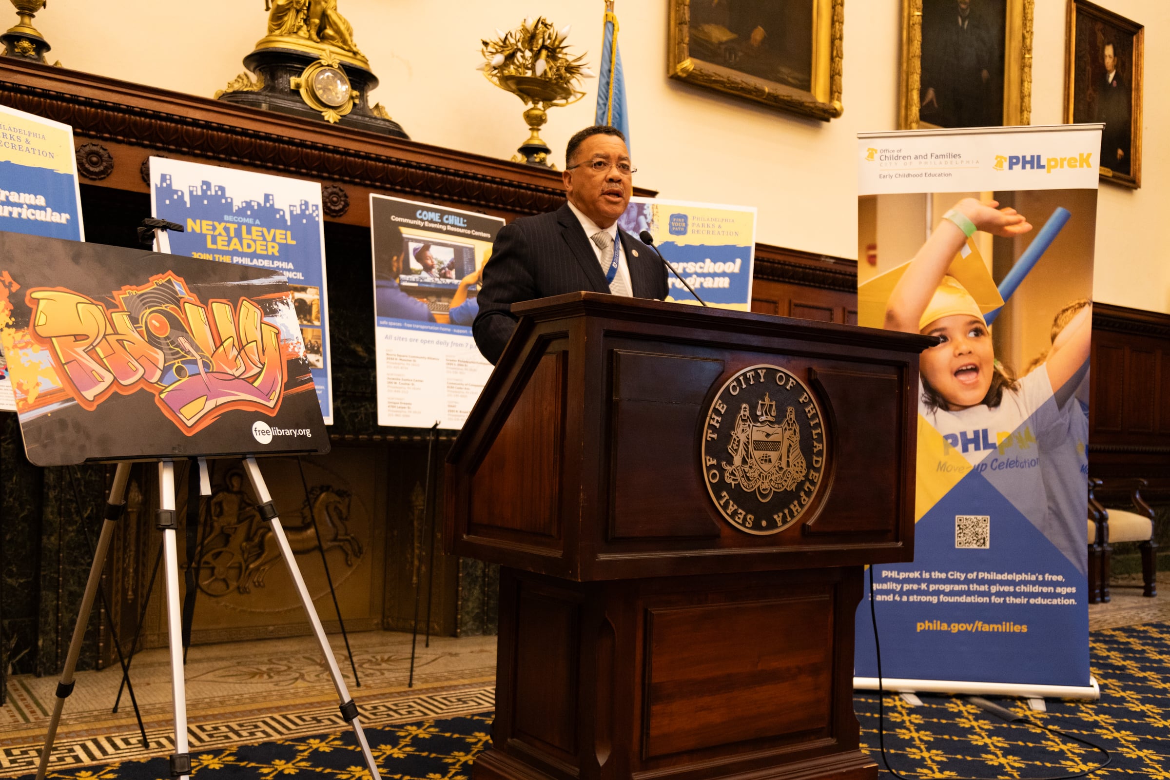 A man in a suit stands at a podium in front of several school safety posters