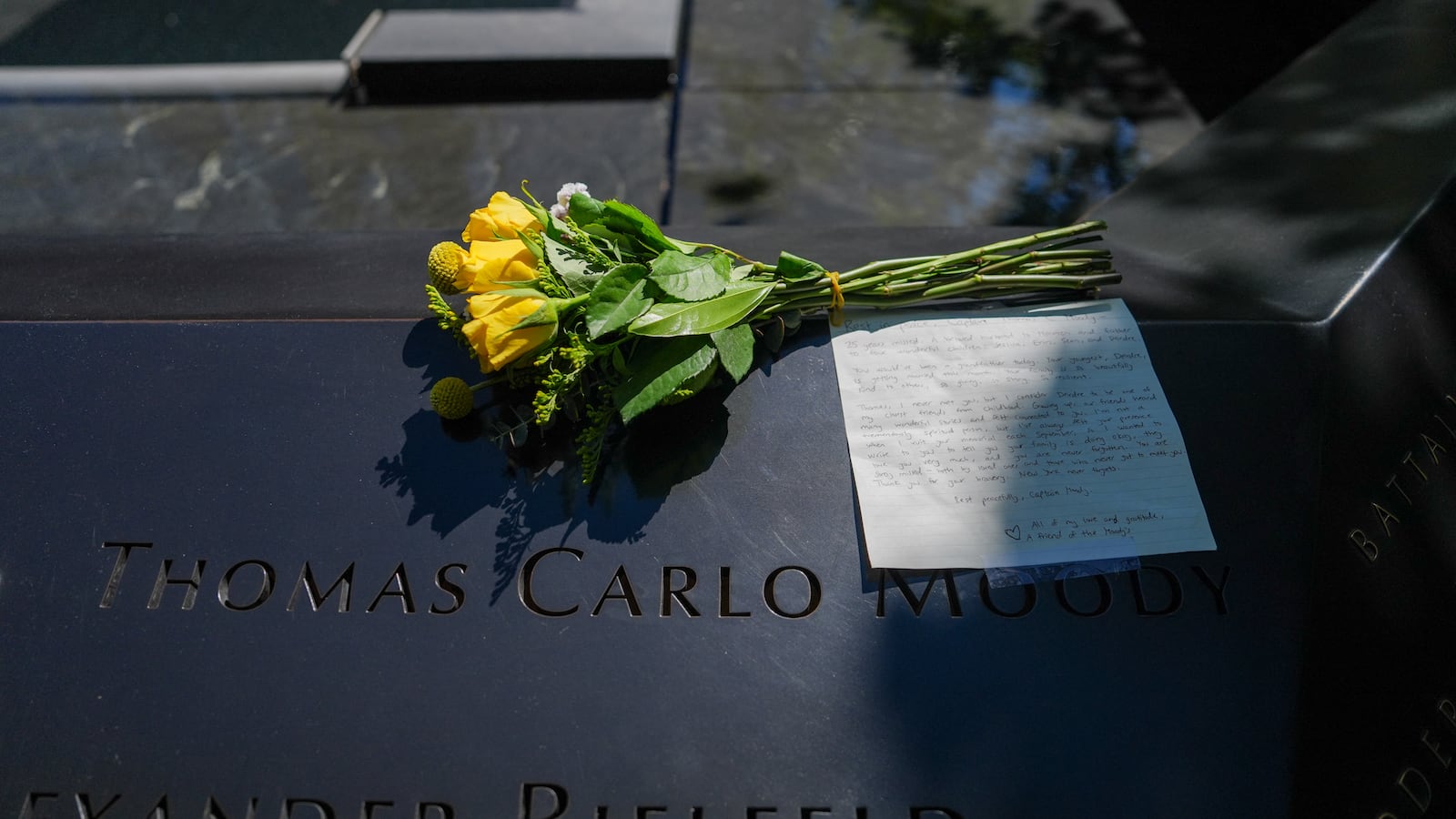 A yellow rose rests near some engraved names.