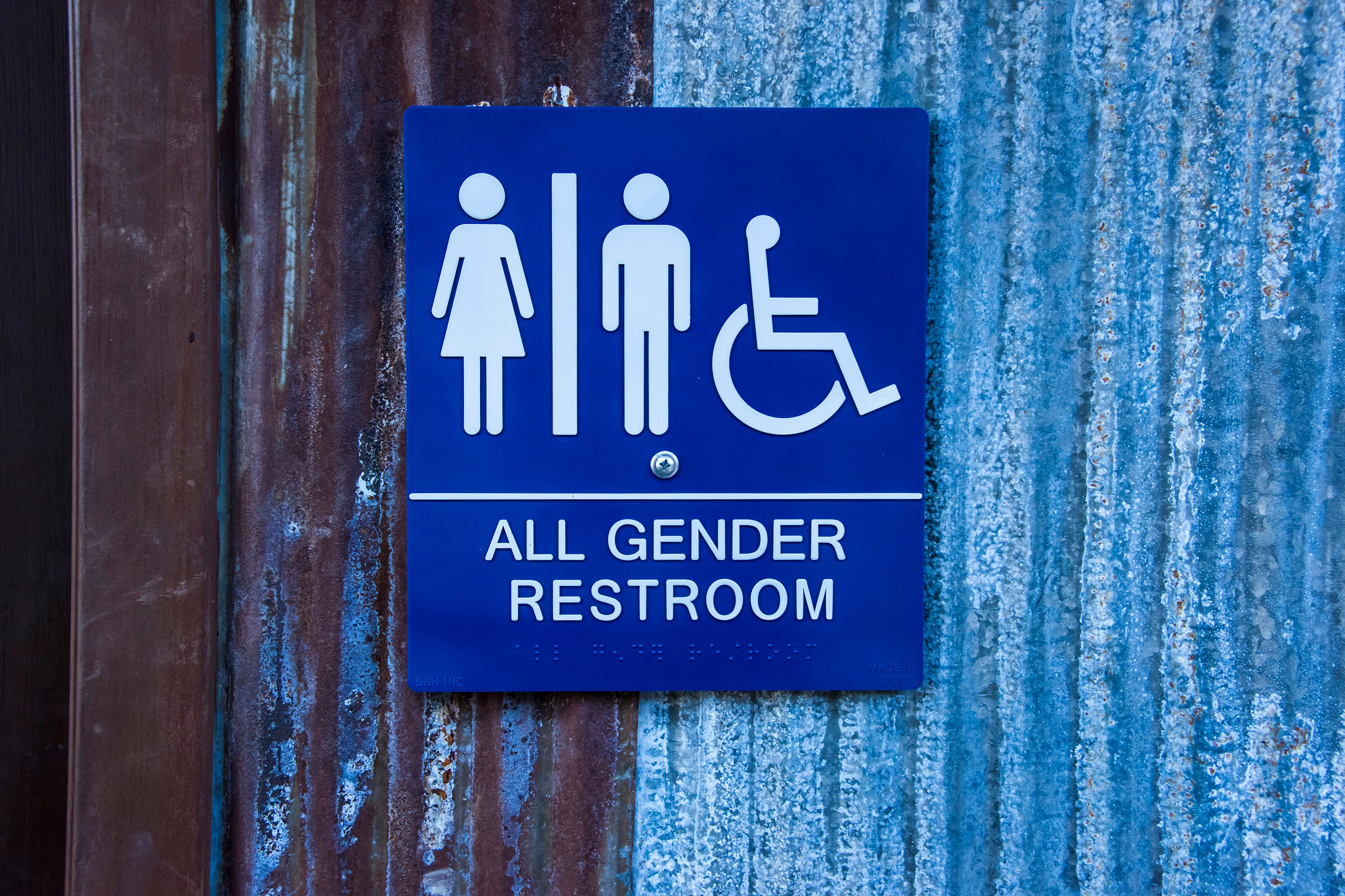 A photograph of a all gender restroom sign against a blue and grey textured wall.