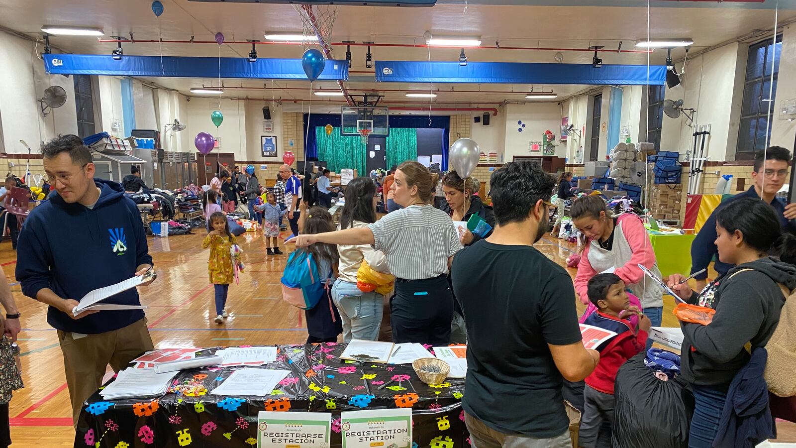 People stand in a school gymnasium full of tables and supplies to give away to families.