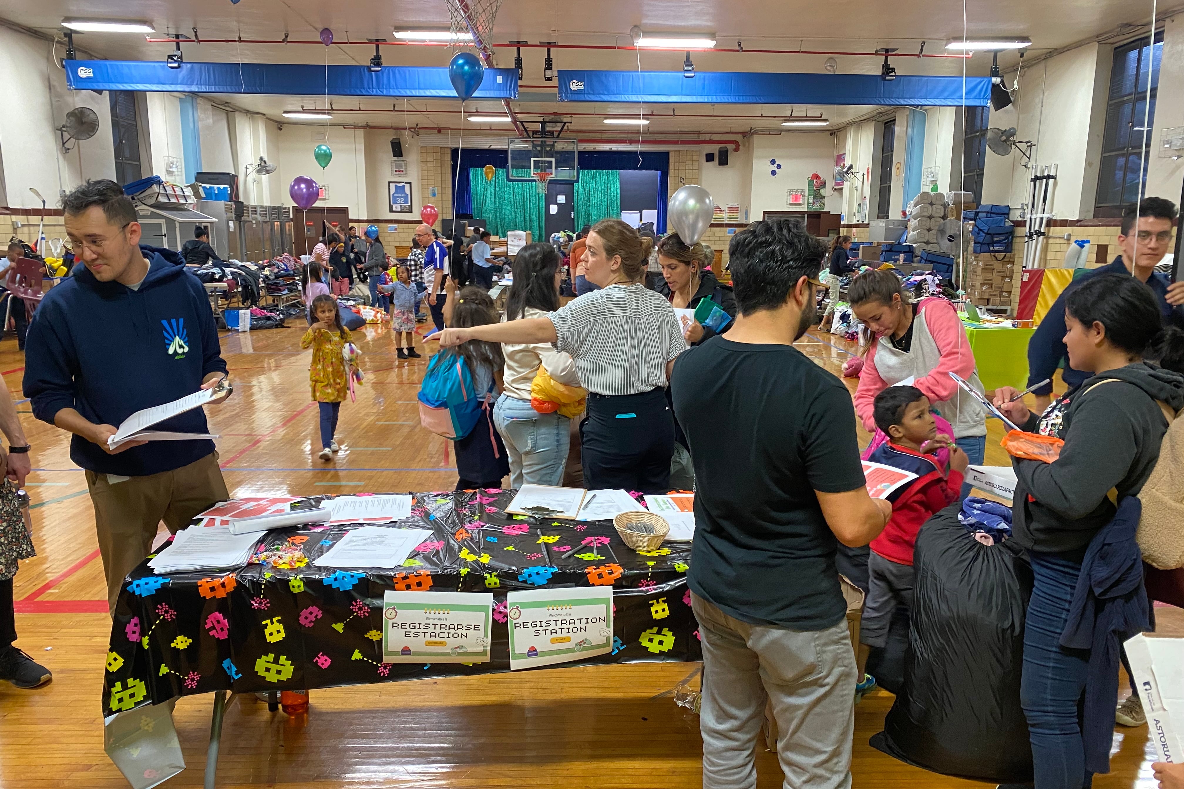 People stand in a school gymnasium full of tables and supplies to give away to families.