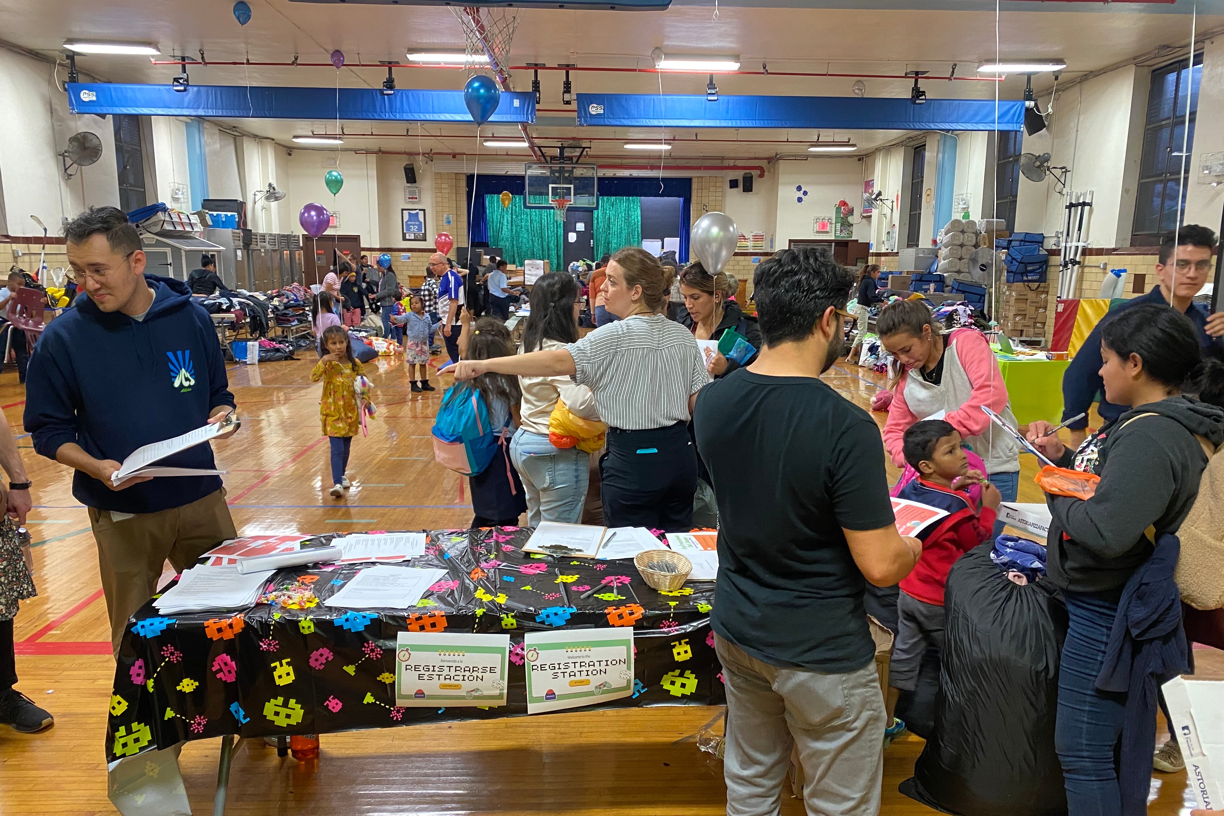 People stand in a school gymnasium full of tables and supplies to give away to families.