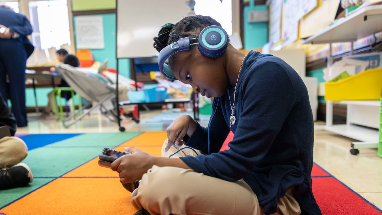 A young girl works on a tablet, wearing blue headphones while sitting on the floor.