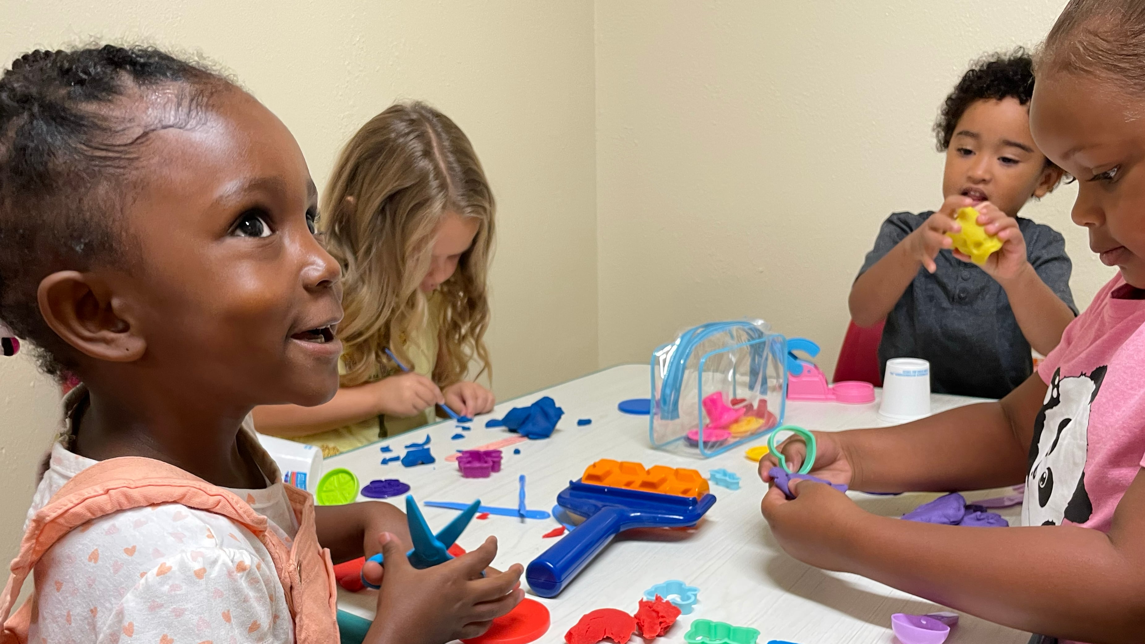 Four young students play with dough and colorful toys at a table.