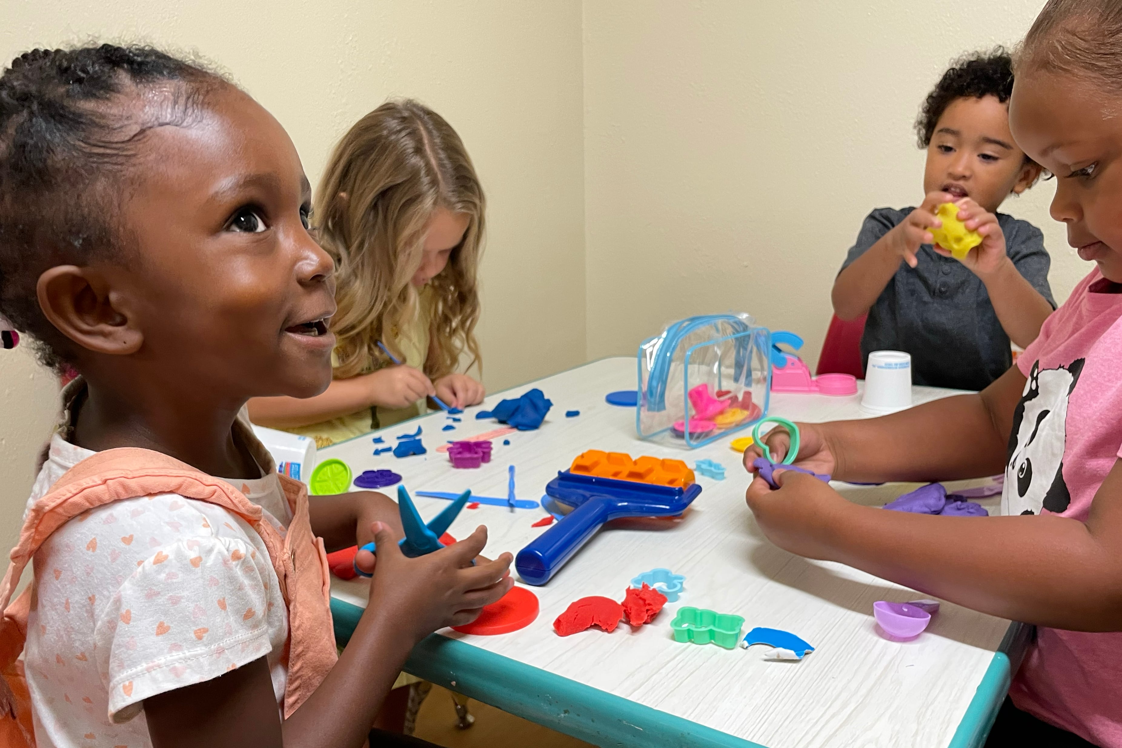 Four young students play with dough and colorful toys at a table.