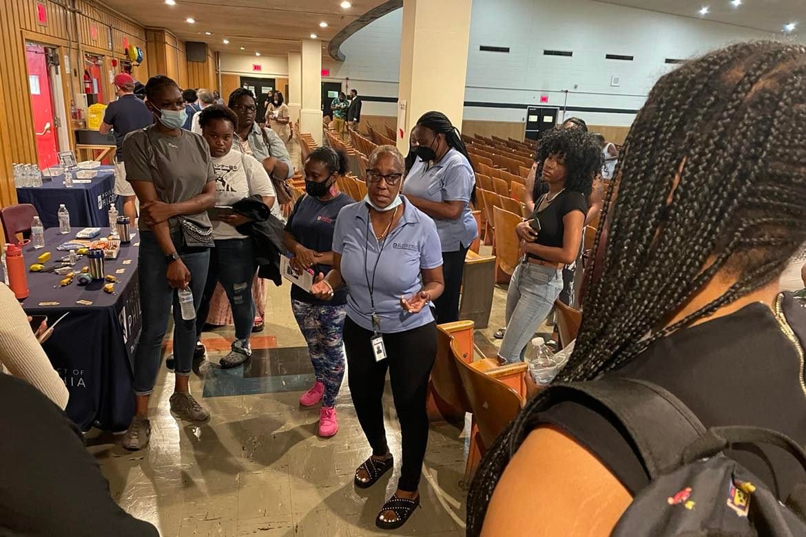 A group of job seekers surround a woman in a blue shirt and black pants at the back of an auditorium at South Philadelphia High School.