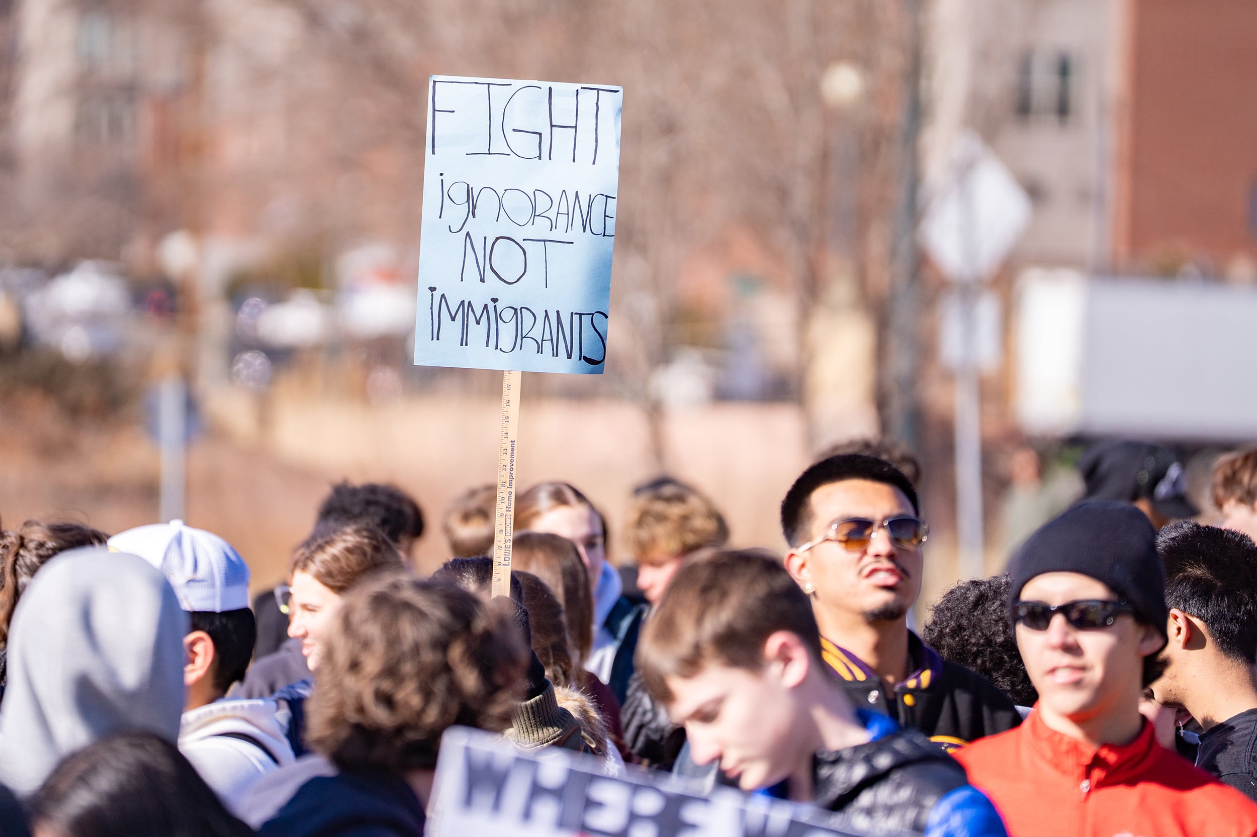 A photograph of a large group of students marching on a sunny day, some are holding protest signs.