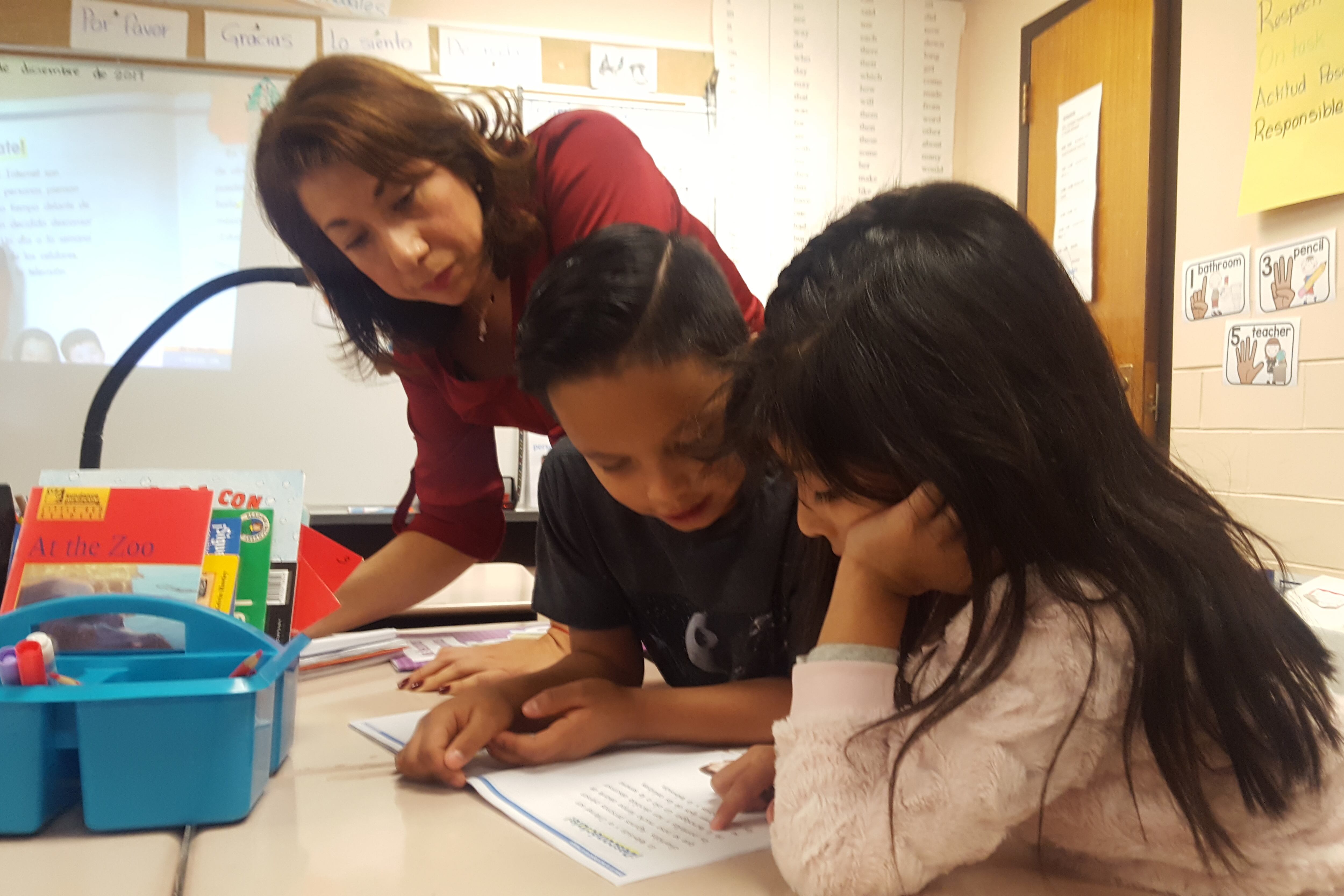 First grade teacher Nancy Carbajal at Dupont Elementary School in Adams 14 listens as students practice reading in Spanish.