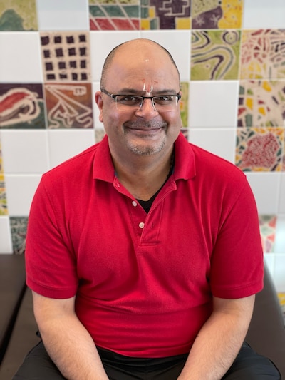 A person with glasses and wearing a red shirt poses for a portrait in front of a quilt.