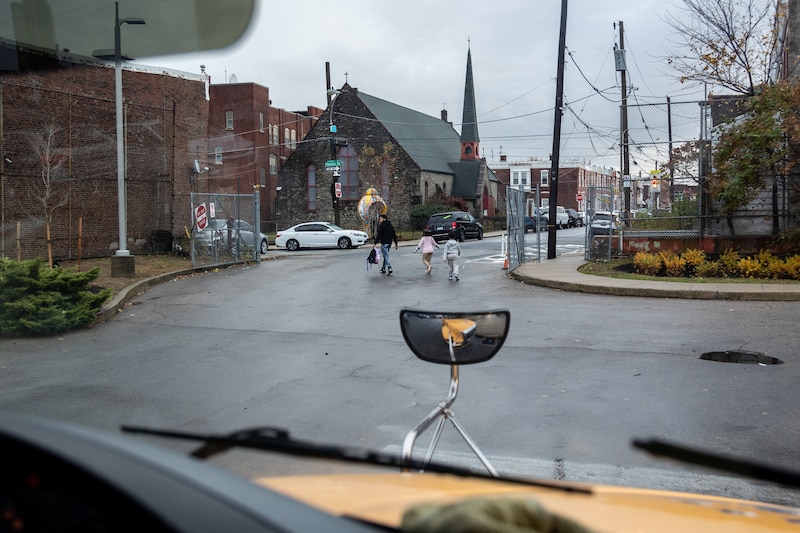 An adult and two students walk across a street.