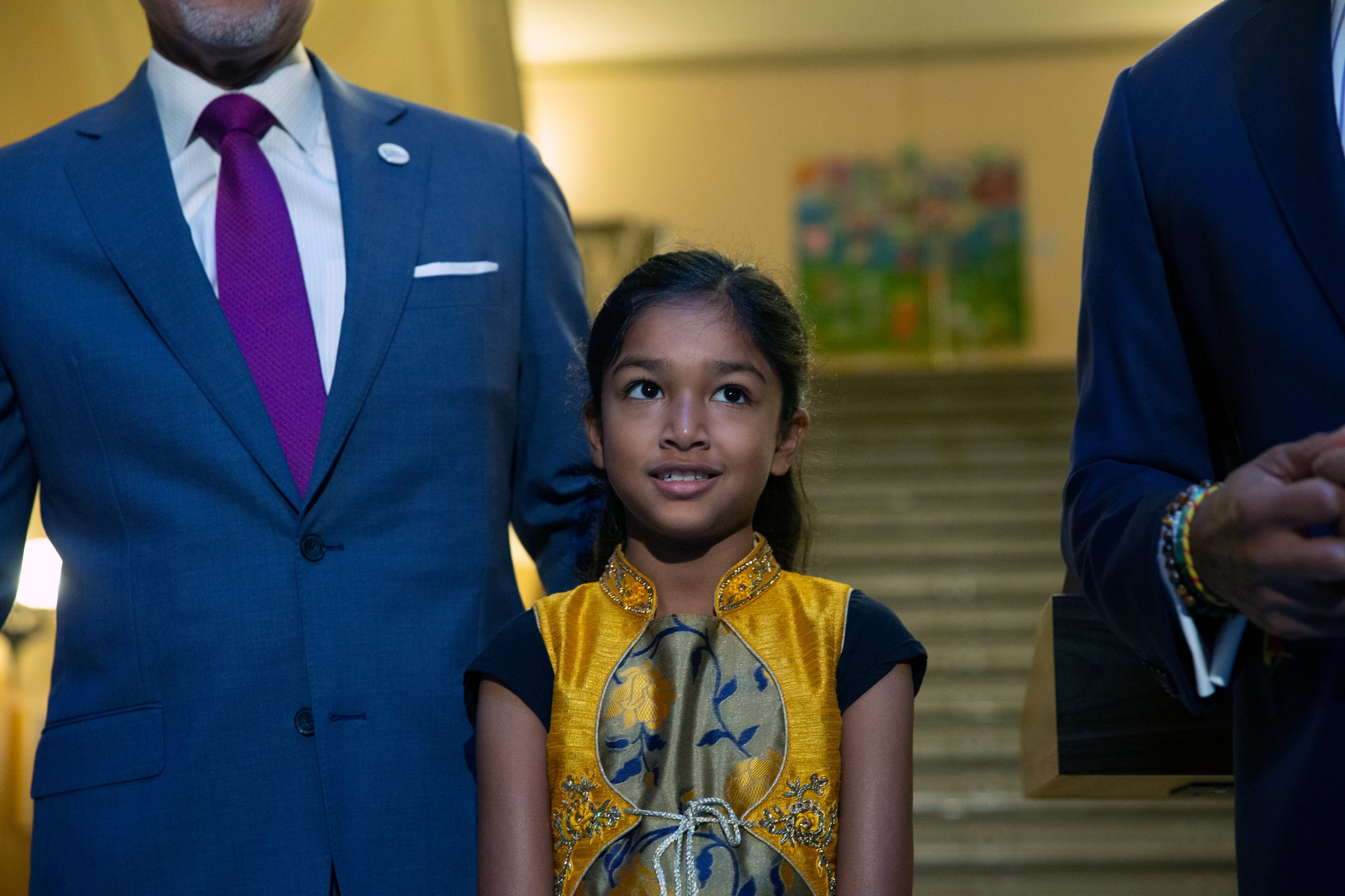 A young student in traditional Southeast Asian dress joined the mayor and schools chancellor to in a rotunda. 