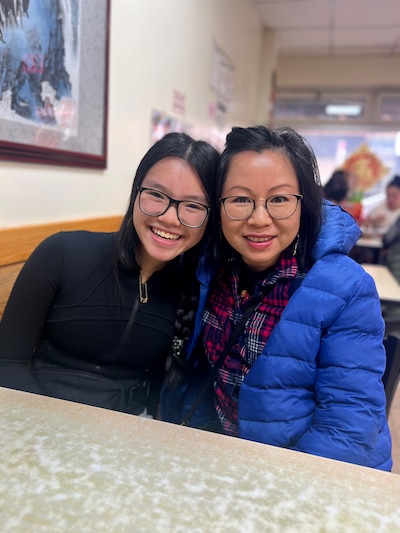 A young girl and a woman sit in a booth at a restaurant while smiling and posing for a photo.