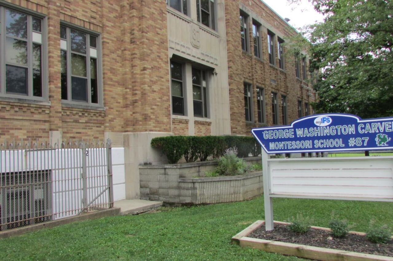 A blue sign that reads “George Washington Carver Montessori School 87” stands in front of a brick building.