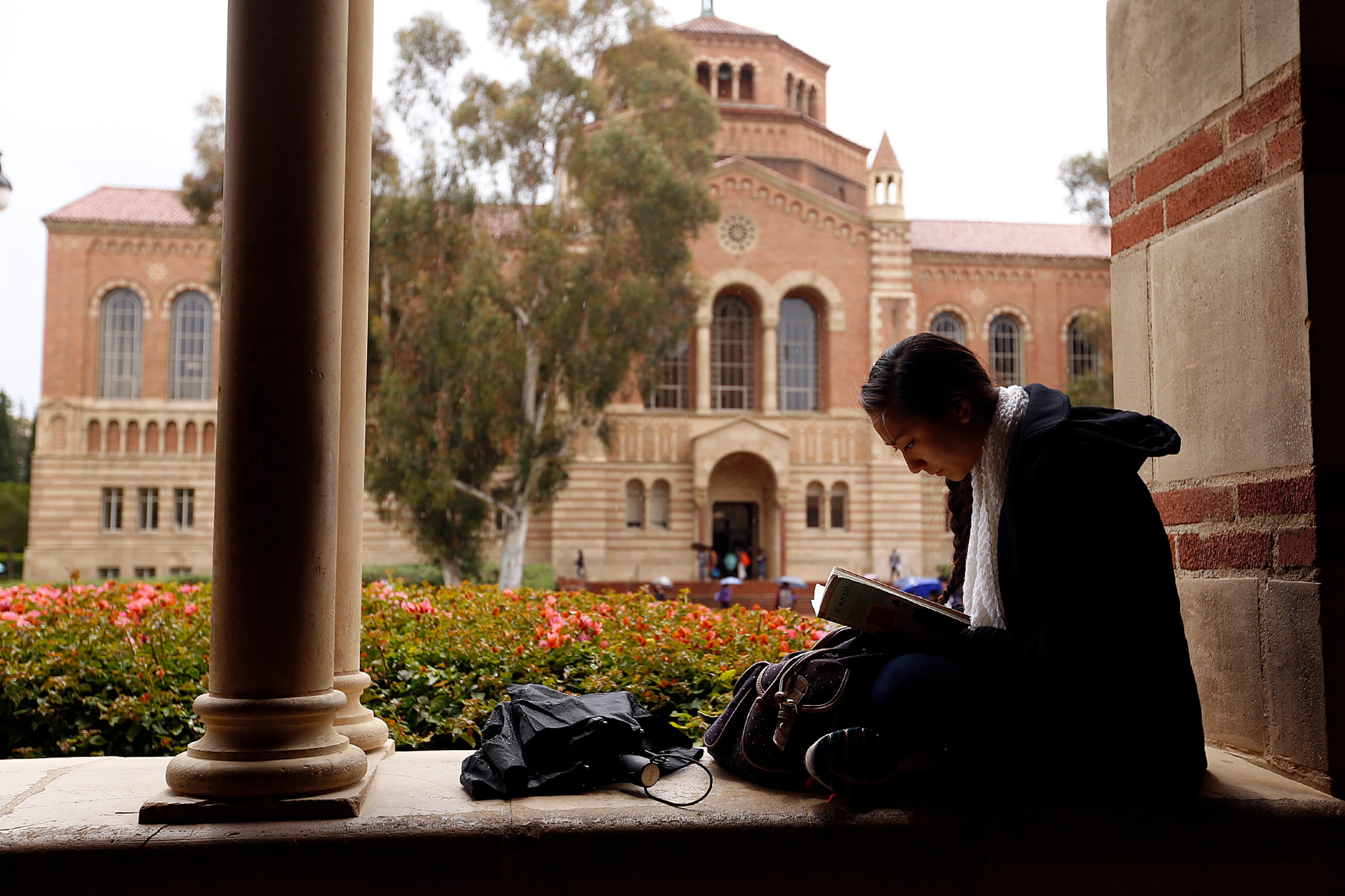 A person is sitting next to a pillar and reading.