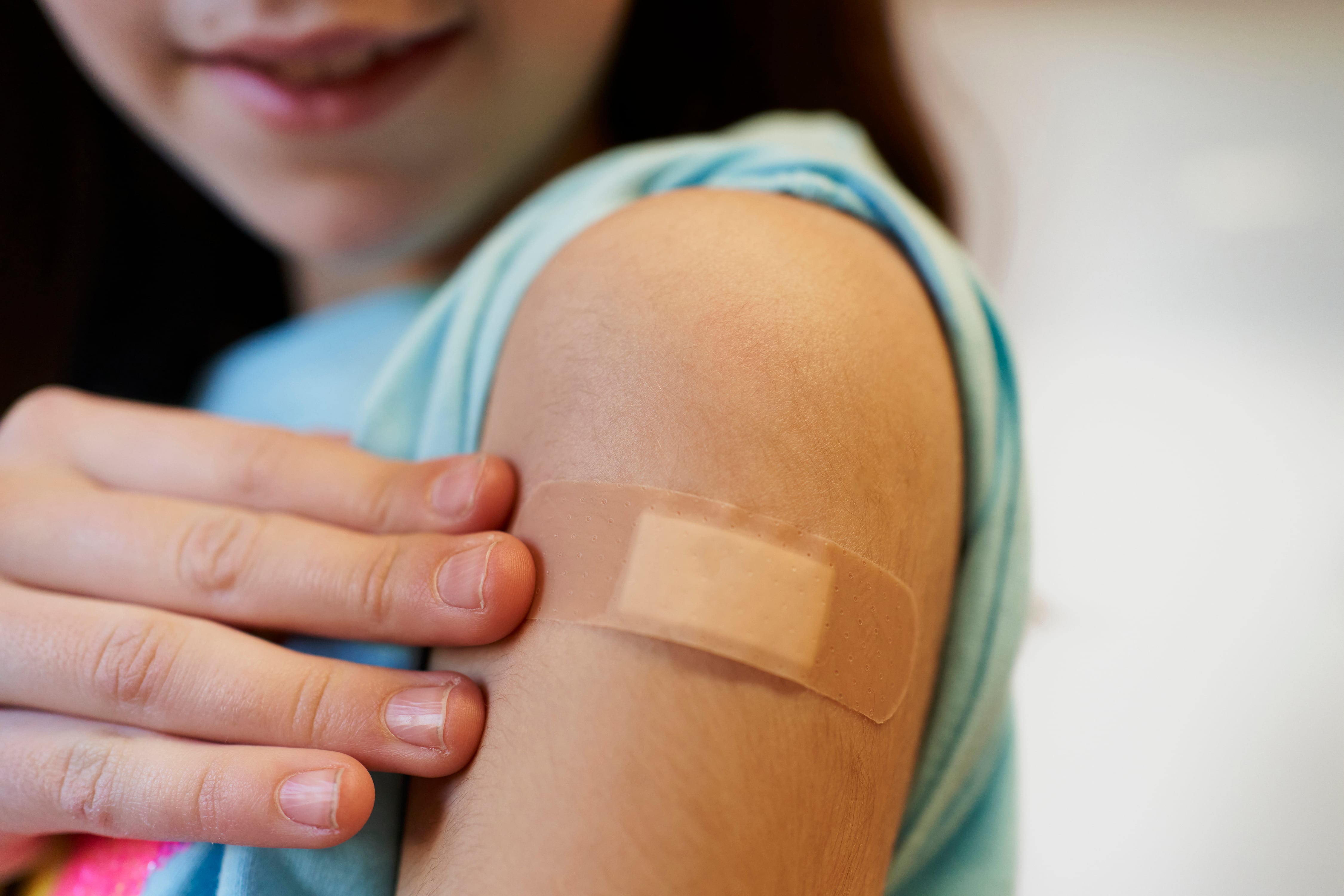 girl points to band-aid on her arm after doctor gives her a vaccine