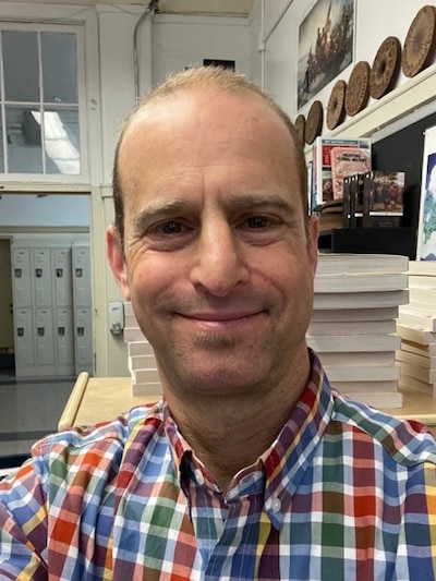 Headshot of a man wearing a red, green, blue and white checked shirt.
