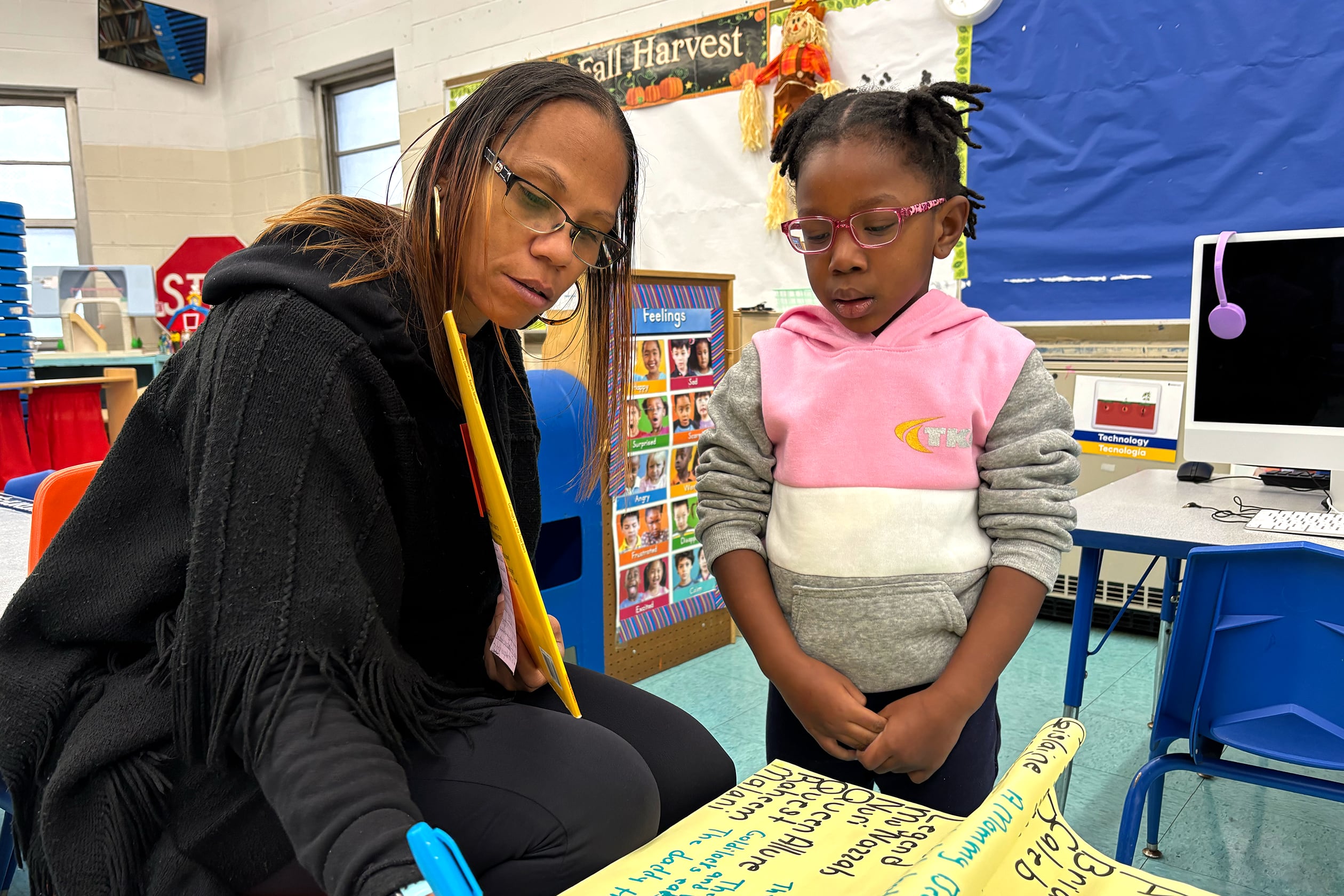 A woman in dark top and pants talks to a female student in a pink, white and gray top.
