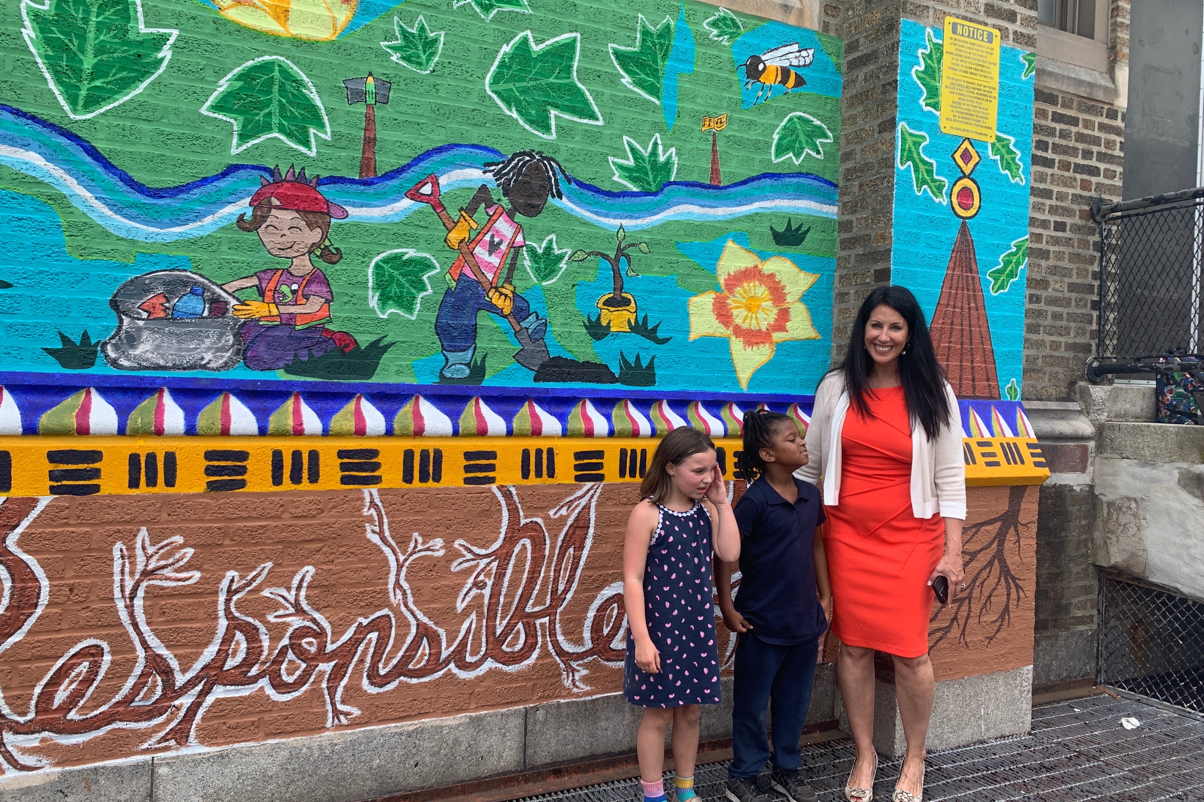 A woman in an orange dress stands in front of a colorful wall mural