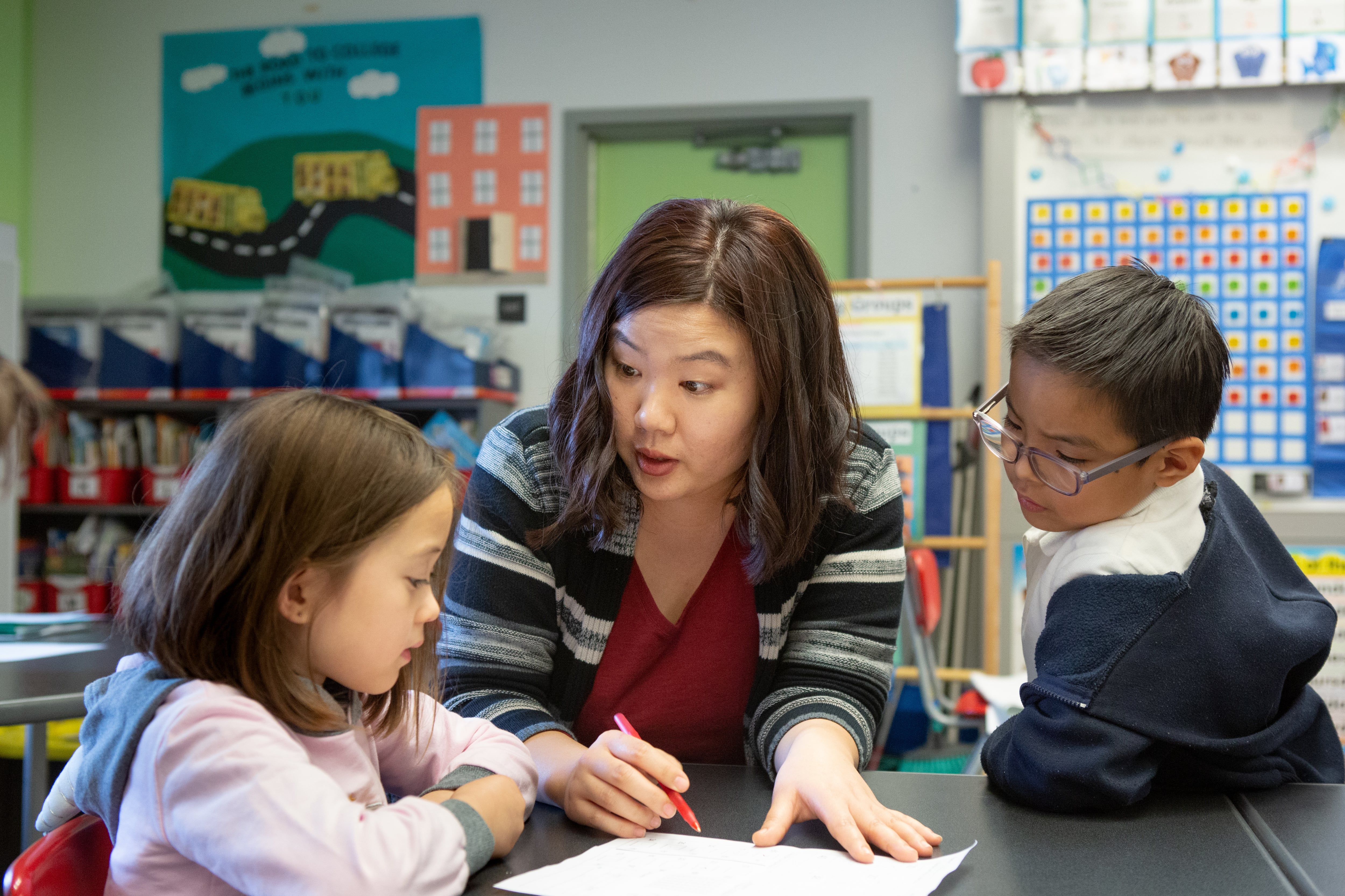 A kindergarten teacher helps a girl and boy with a class activity.