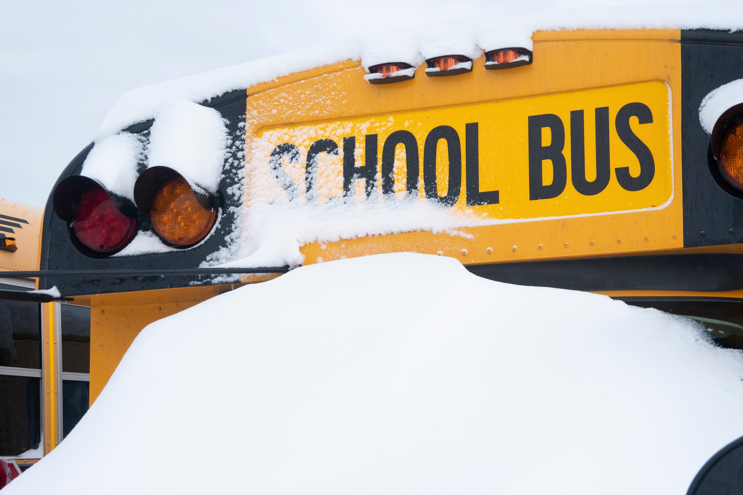 A photograph of a snow covered yellow school bus on a cloudy day.