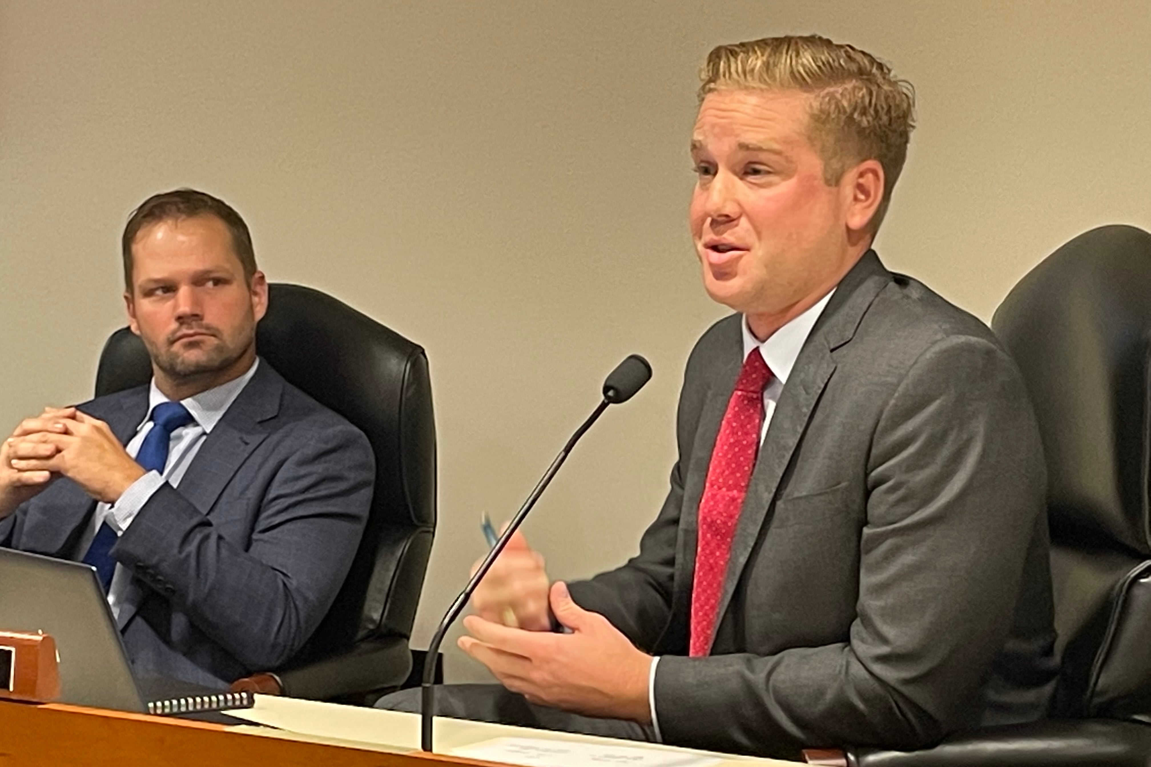 Republican state Rep. Andrew Beeler speaks in front of a microphone in a committee room while Republican Rep. Bryran Posthumus looks on.
