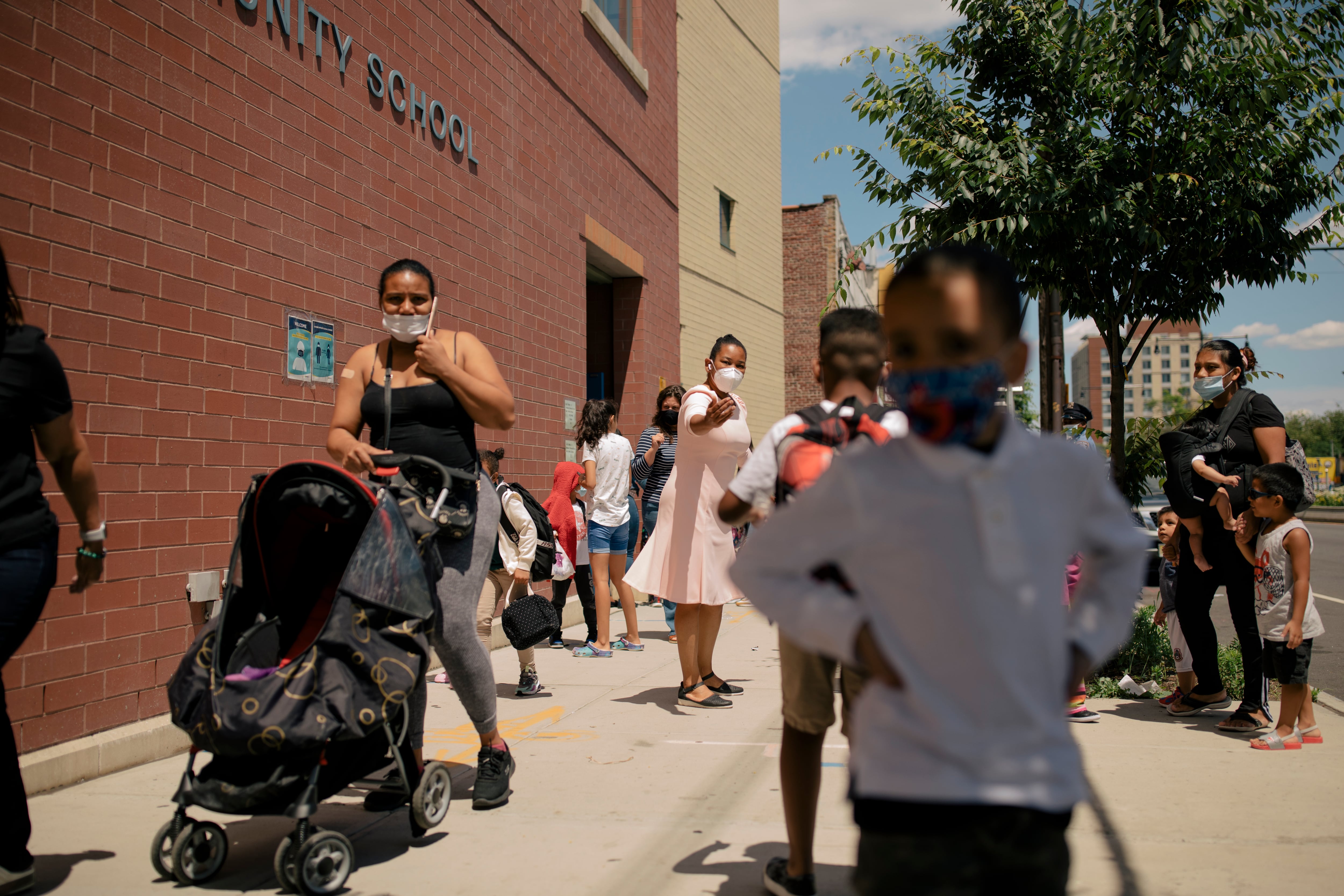 Students walk outside a school in Brooklyn. The school is brick, and a young student in a white shirt is in the foreground.